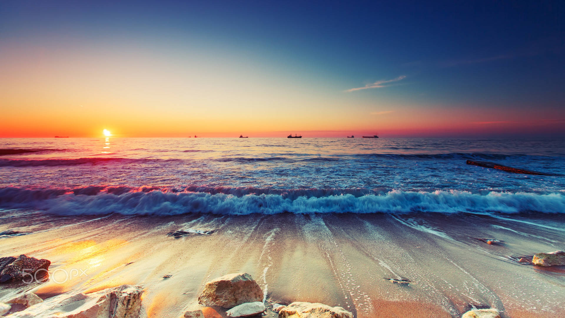 夕陽下的海洋，海浪拍打沙灘，遠處有船隻