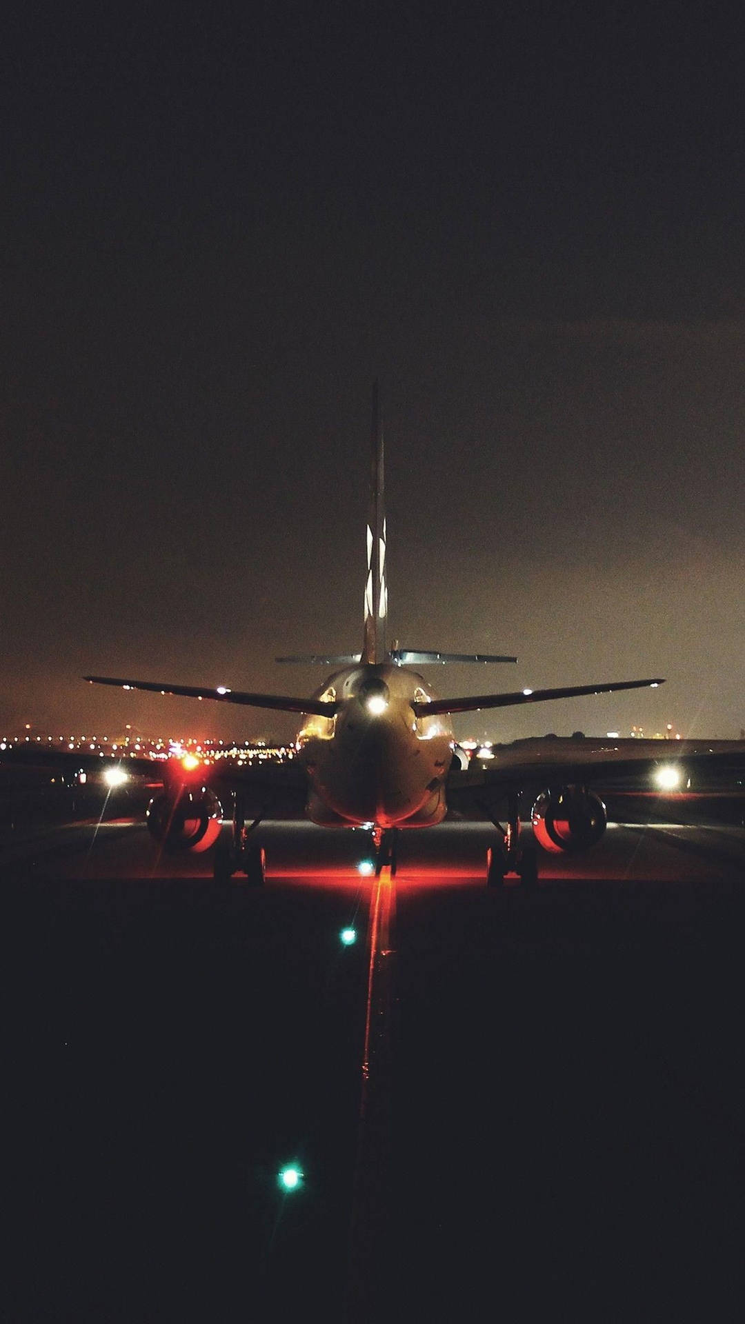 夜間飛機在跑道上的正面視圖，遠處有城市燈光。
