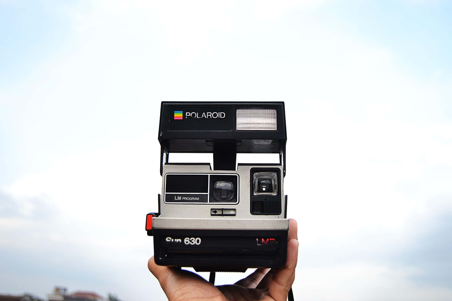 手拎住Polaroid Sun 630即影即有相機，背景係多雲天空。