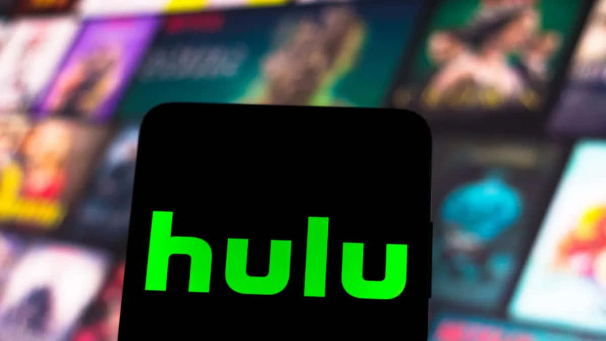 即時觀看 Hulu 最新電影與劇集 壁紙 — 一部智能手機清晰顯示亮綠色Hulu標誌，背景是模糊的彩色串流服務縮圖。