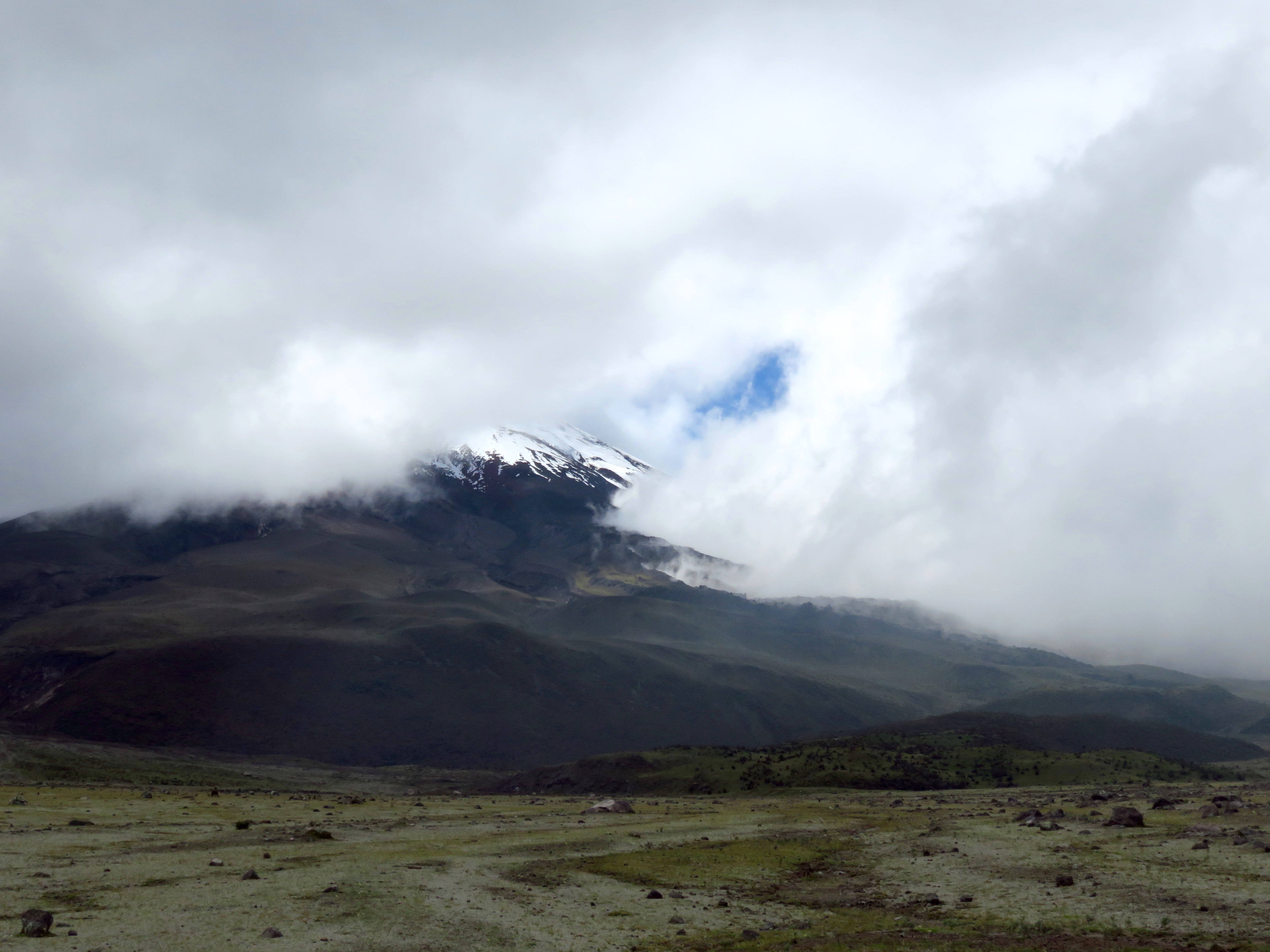 厄瓜多爾科托帕克山步道 壁紙 — 白雪覆蓋的山峰穿透厚雲，出現在廣闊的綠色和棕色谷底之上。