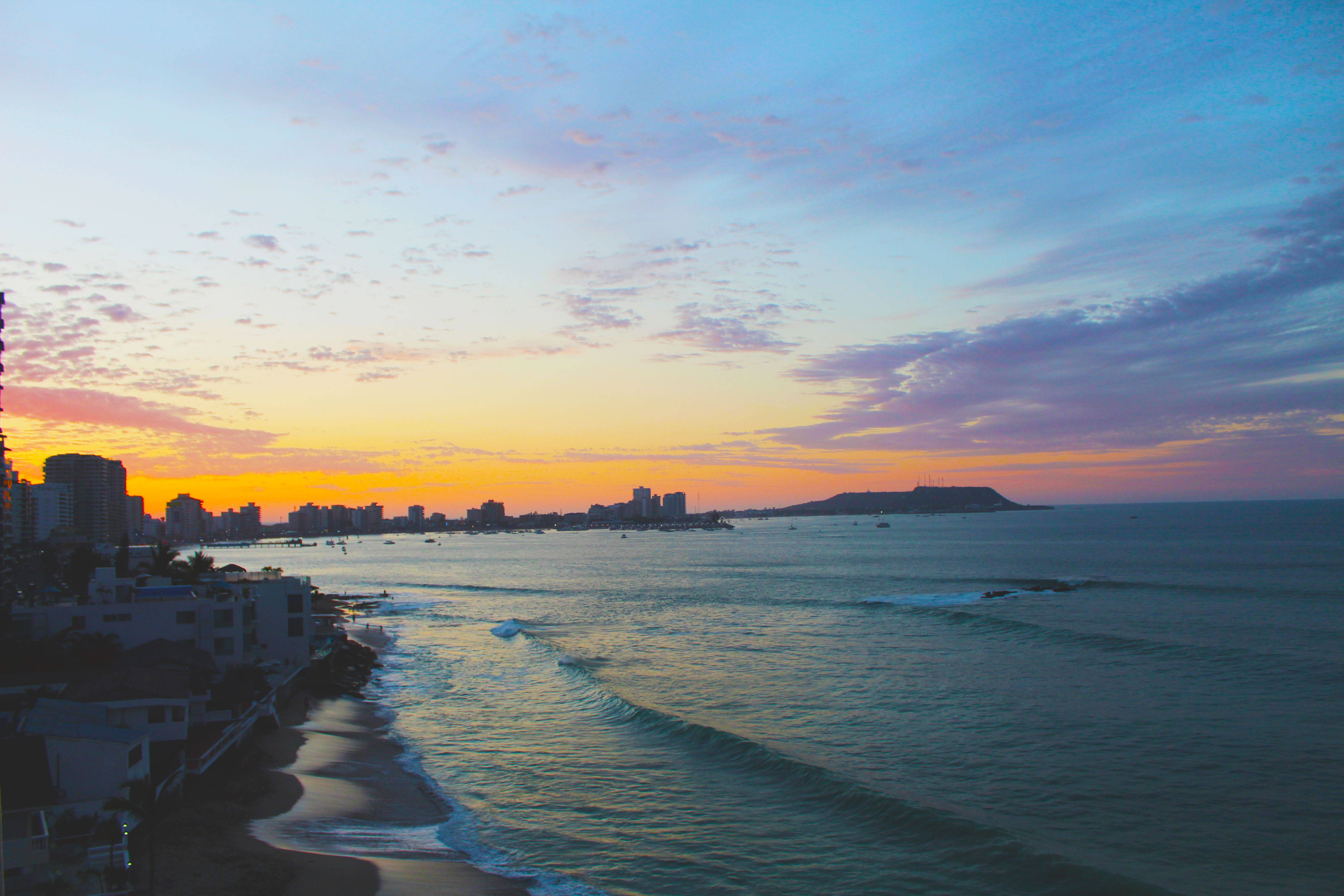 厄瓜多爾薩利納斯海岸 壁紙 — 夕陽將天空染成橙色和紫色，海浪拍打著城市天際線旁的海灘。