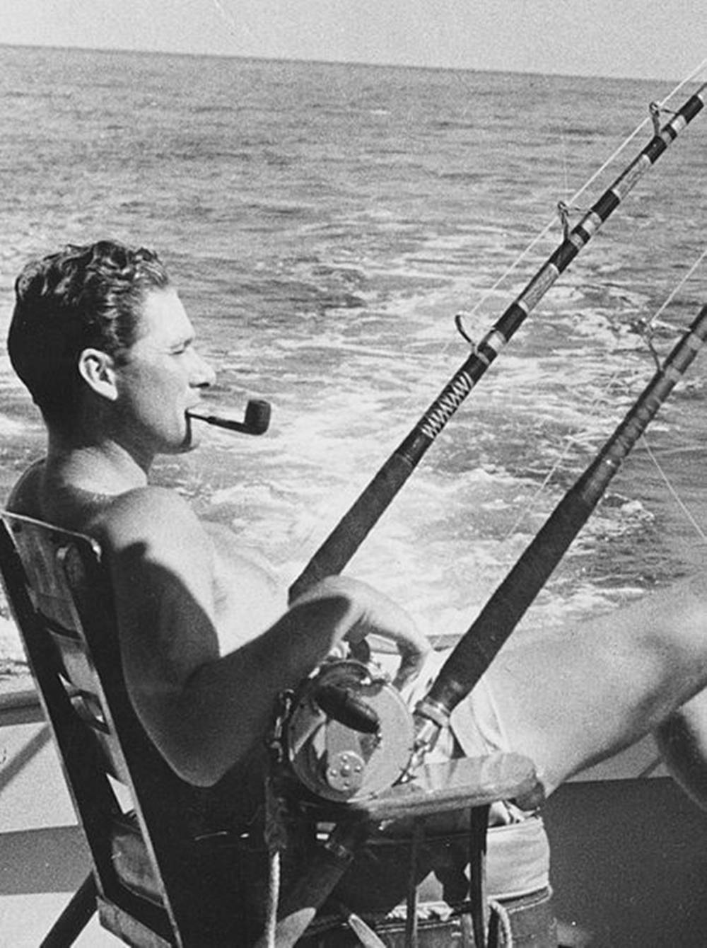 男子抽煙斗在海洋上從船上釣魚