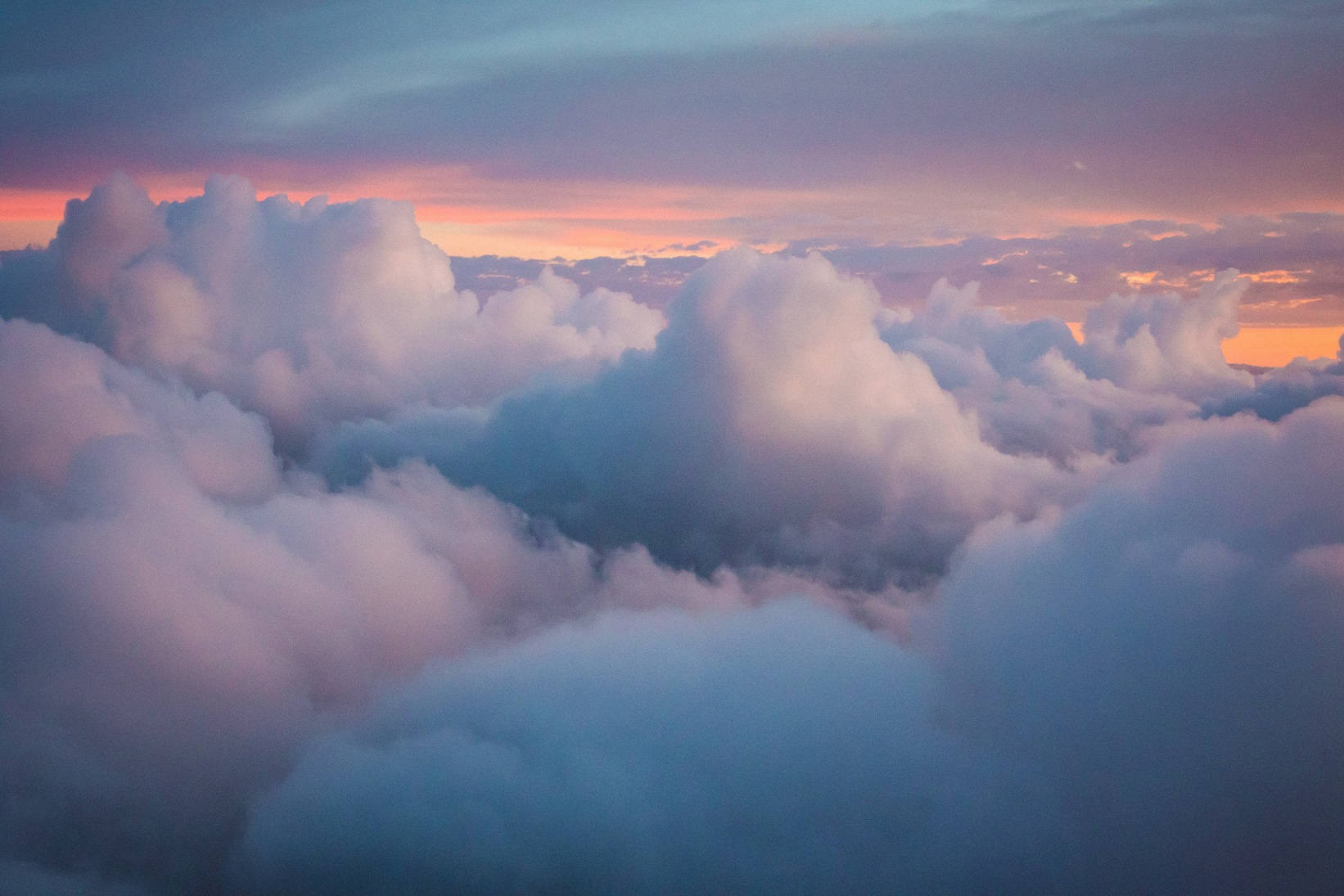 厚積雲與唯美天空 壁紙 — 從高空俯瞰，蓬鬆的雲朵在寧靜的日出時分沐浴在柔和的粉紅和藍色調中。