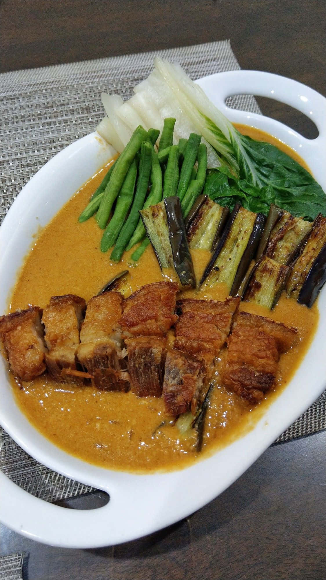 厚花生醬炸肉燉菜 壁紙 — 白色碟子盛載著脆皮豬腩肉，配以濃郁的橙咖哩醬汁、青豆和茄子，並以菠菜點綴。