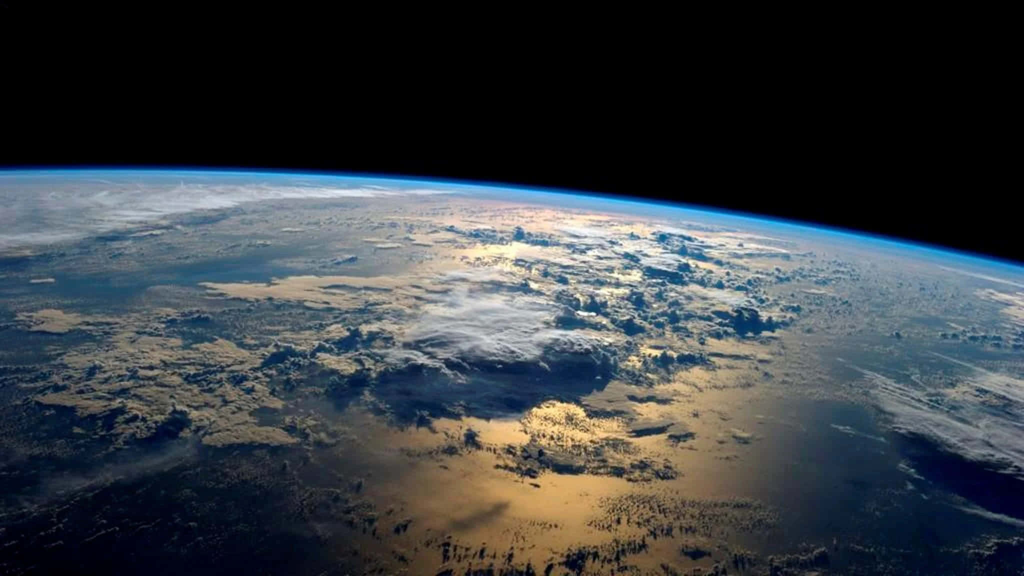 厚重雲層覆蓋地球背景 壁紙 — 從太空觀看地球，金色陽光照亮藍色海洋和陸地上的雲層。