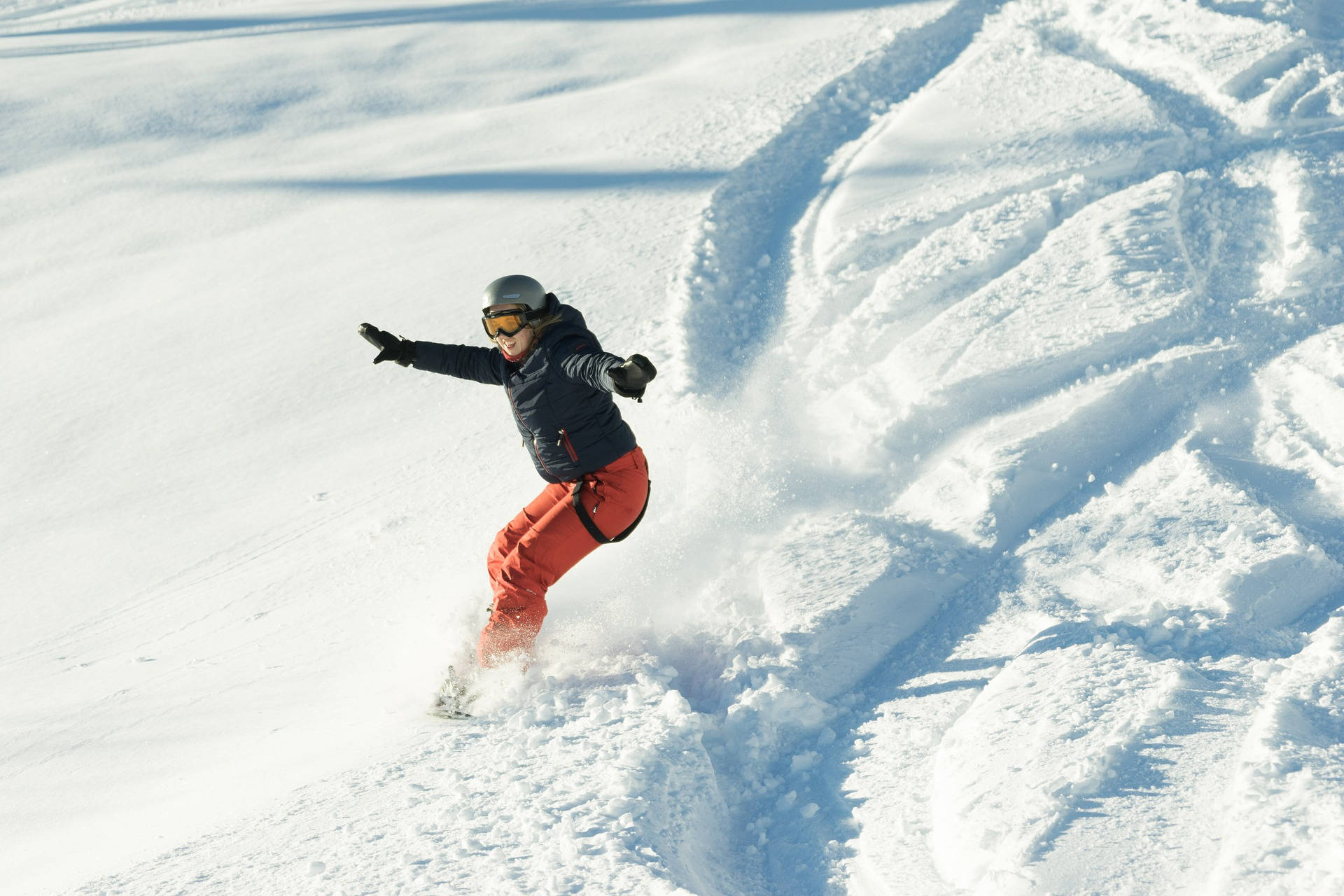 滑雪板運動員穿著亮橙色褲子從白雪覆蓋的山坡滑下。