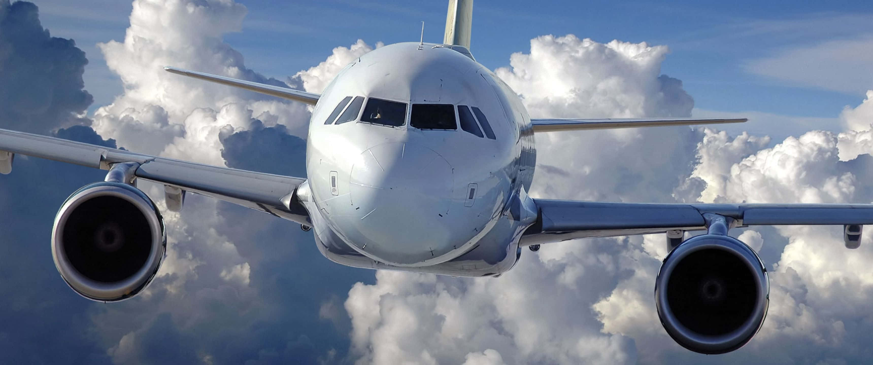 厚雲繚繞的巨型客機 3440x1440p 背景 壁紙 — 一架白色客機在明亮的藍天中翱翔於蓬鬆的白雲之間。