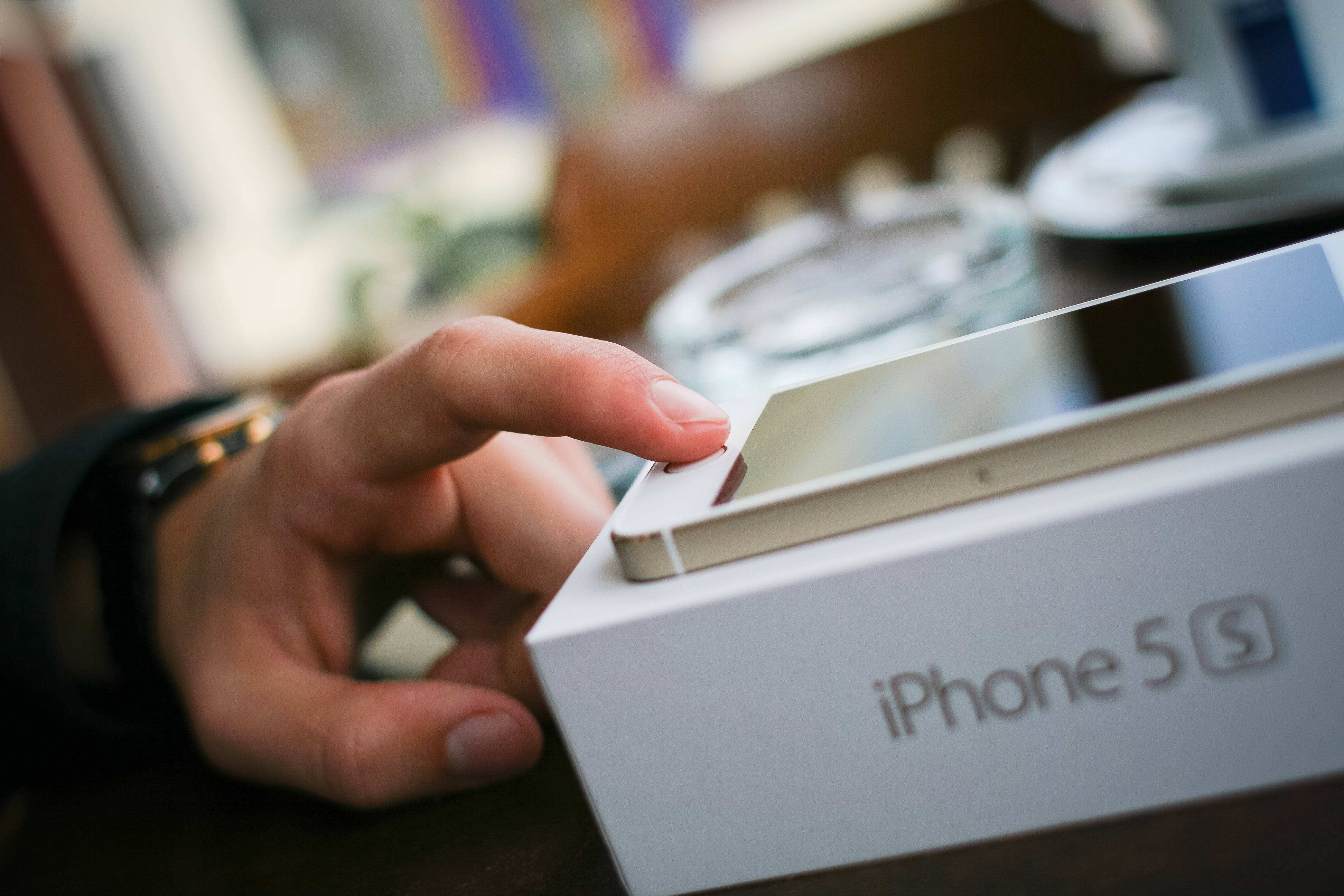 原裝 iPhone 5 S 指紋辨識 壁紙 — 一隻手輕輕揭開白色 iPhone 5s 盒子的蓋子，露出裡面時尚的銀色手機。