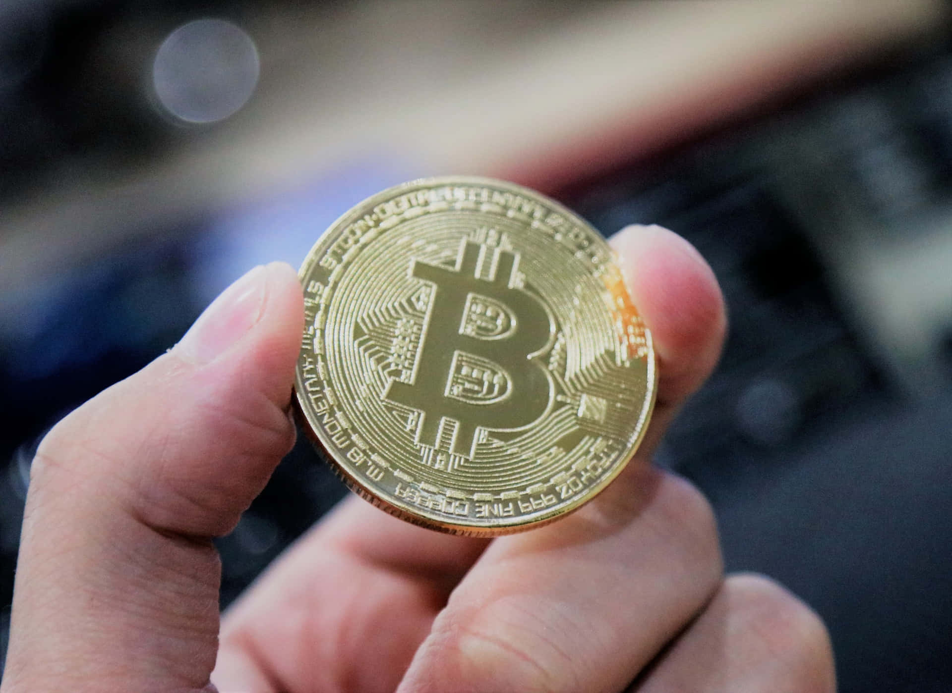 去中心化貨幣的未來 壁紙 — 一隻手拿著一枚閃閃發光的金色比特幣硬幣，上面有電路圖案，背景是模糊的科技背景。
