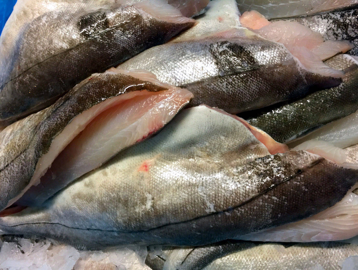 去頭去骨鱒魚特寫 壁紙 — 新鮮魚柳帶有閃亮銀鱗和粉紅肉質，放在市場攤位的碎冰上。
