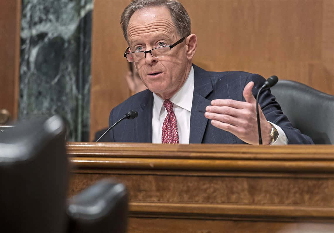 參議員Pat Toomey在委員會會議中熱情發言 壁紙 — 一名身穿西裝戴眼鏡的男子在設有咪高峰的木製聆訊桌上認真發言。