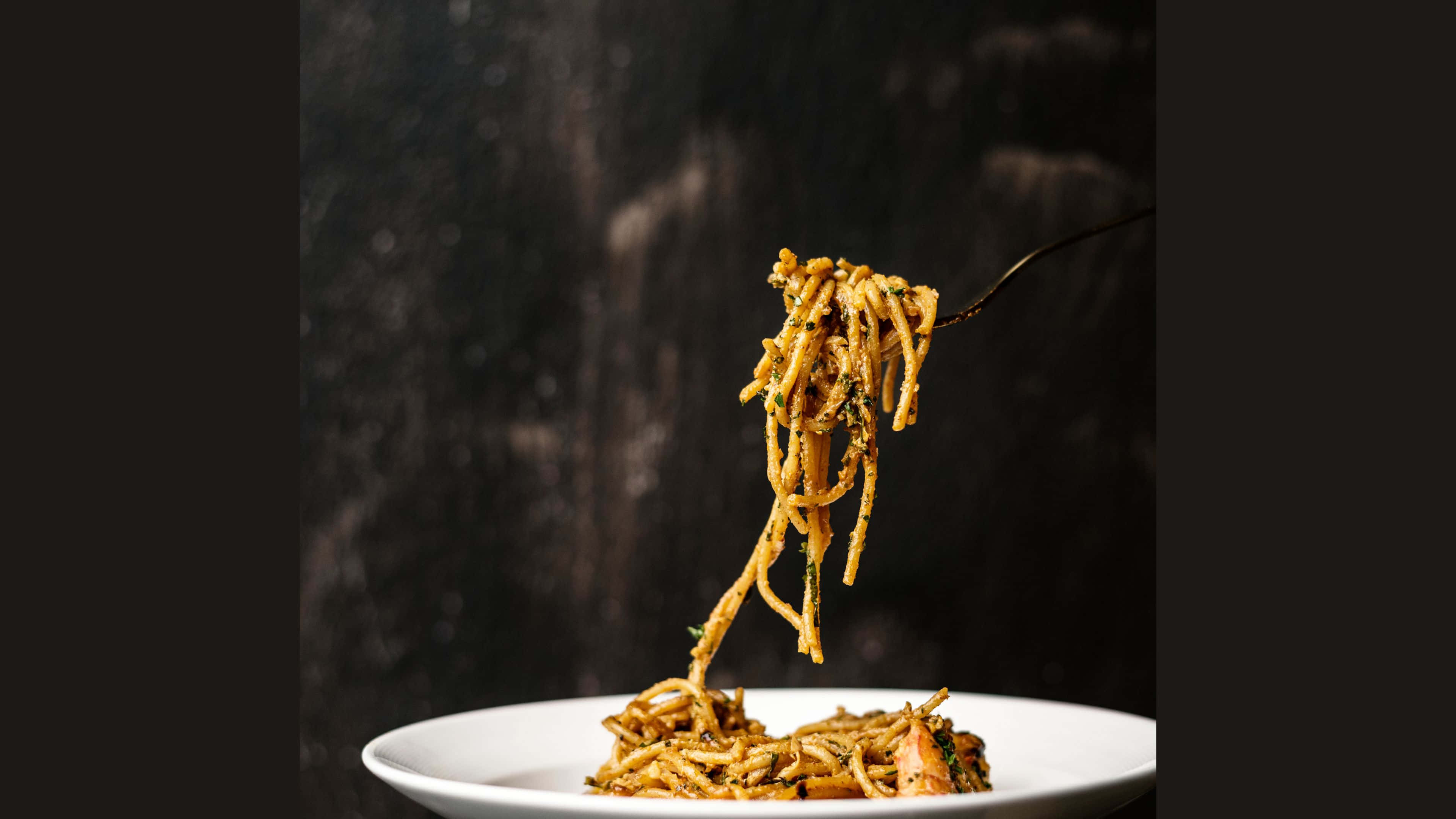 Noodles 桌布 壁紙 — 叉子將金黃色的意大利麵條連同香草從深色紋理背景中挑起。