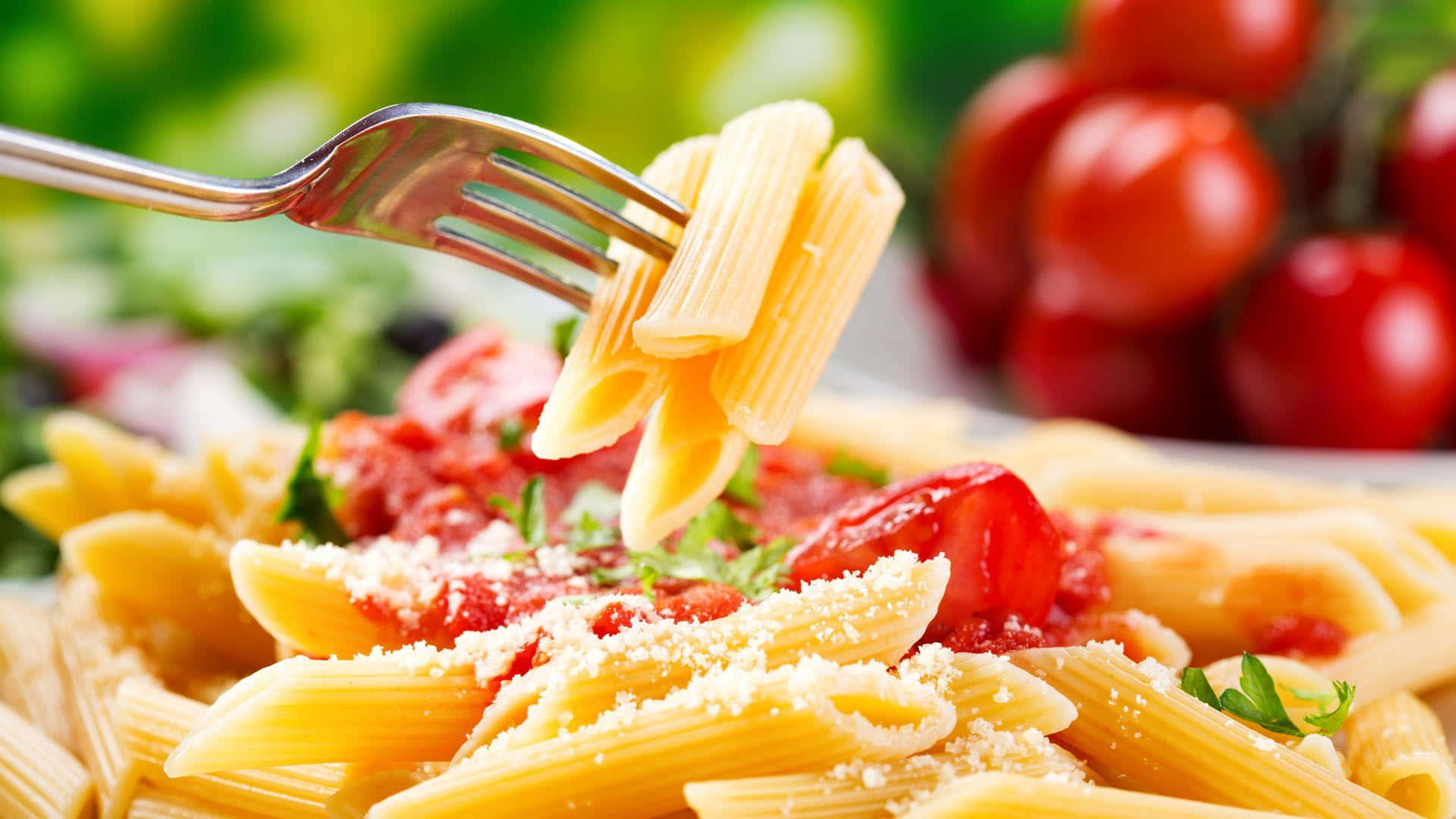 Pasta 桌布 壁紙 — 叉子正在提起沾滿鮮豔番茄醬並撒上磨碎芝士的金色長通粉，背景是模糊的綠色和紅色。