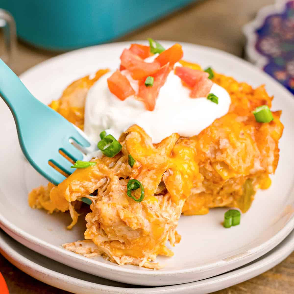 叉子舀起 enchiladas 盤中盛放 壁紙 — 芝士雞肉玉米餅砂鍋菜的特寫，上面放有酸奶油、番茄粒和青蔥，放在白色碟子上，配藍色叉子。