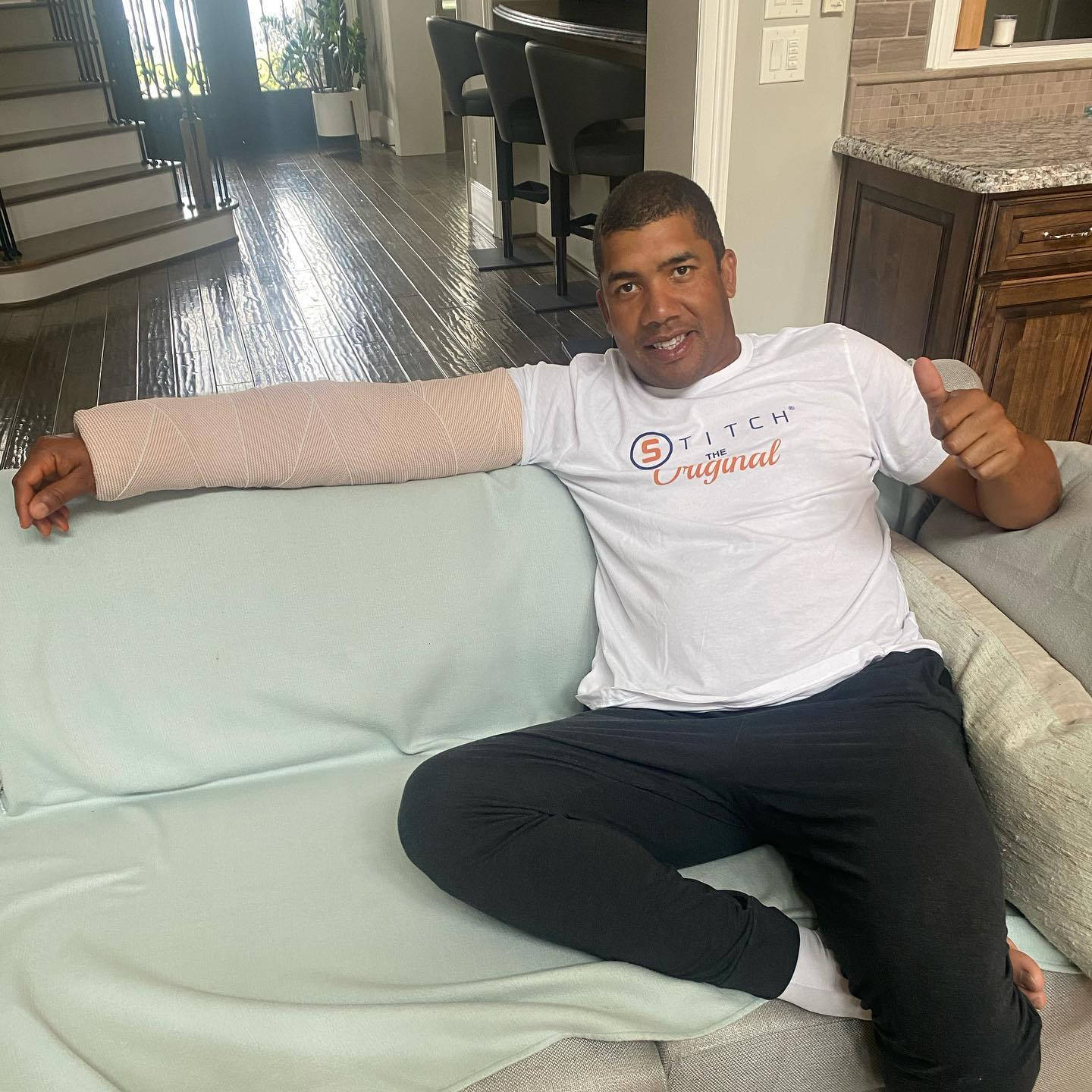 受傷仍堅毅的 Jhonattan Vegas 比出大拇指 壁紙 — 一個手臂打石膏的男人坐在現代家居的沙發上豎起大拇指。