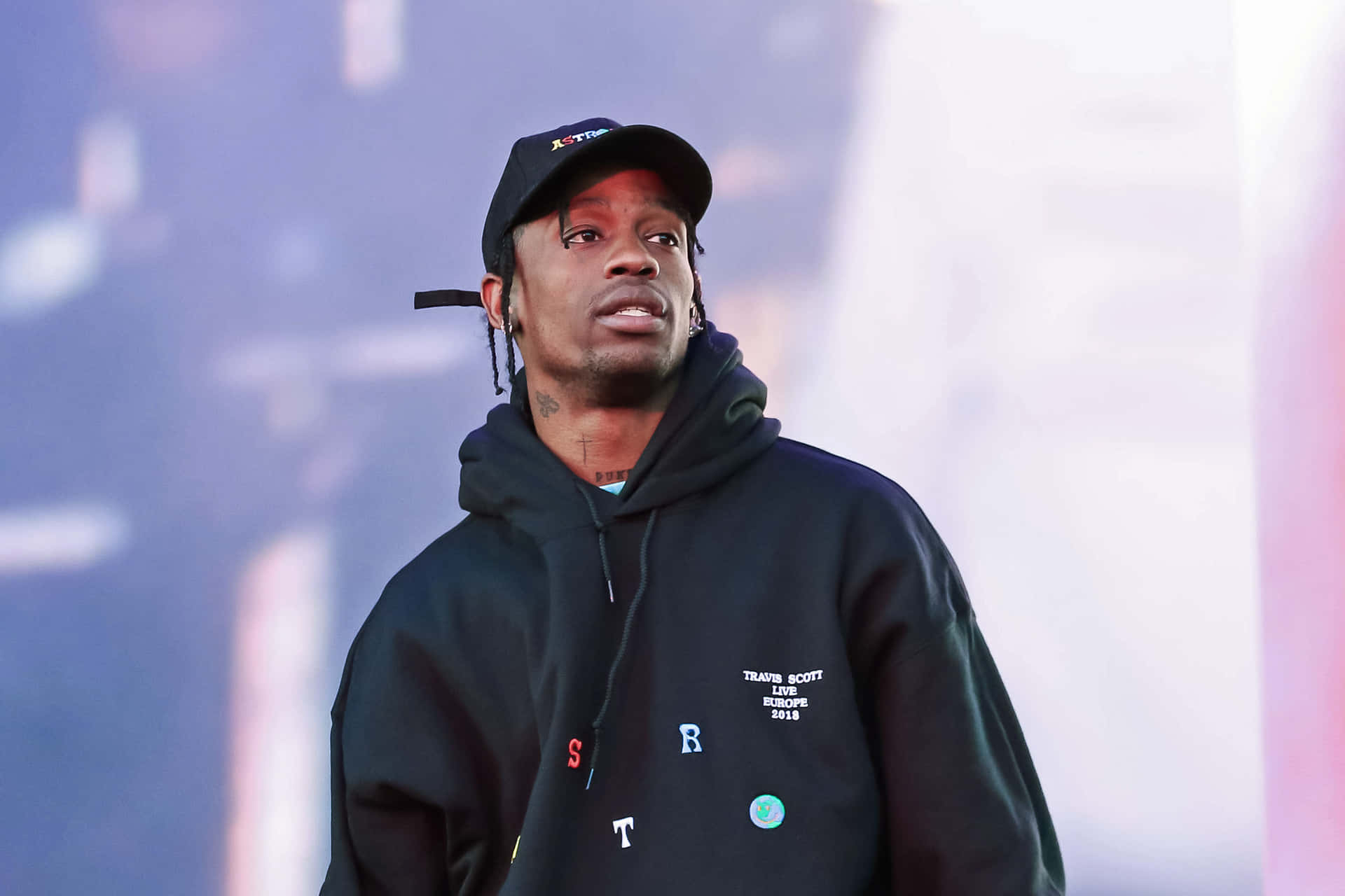 Travis Scott 在彩色燈光下身穿黑色連帽衫和帽子在舞台上表演。