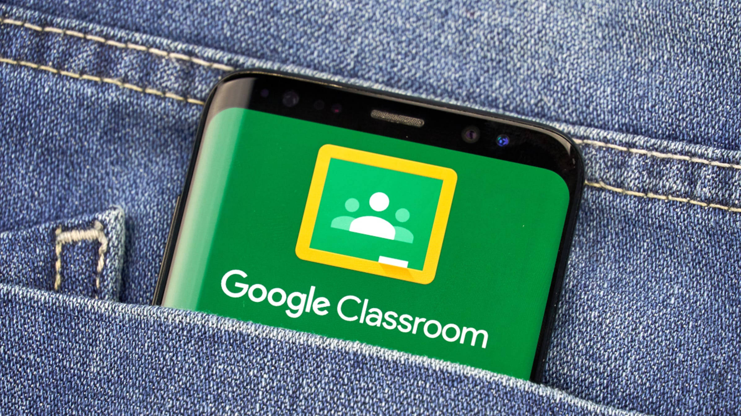 口袋中手機顯示 Google Classroom 應用 壁紙 — 一部顯示 Google Classroom 應用程式的智能手機從藍色牛仔褲口袋中探出頭來。