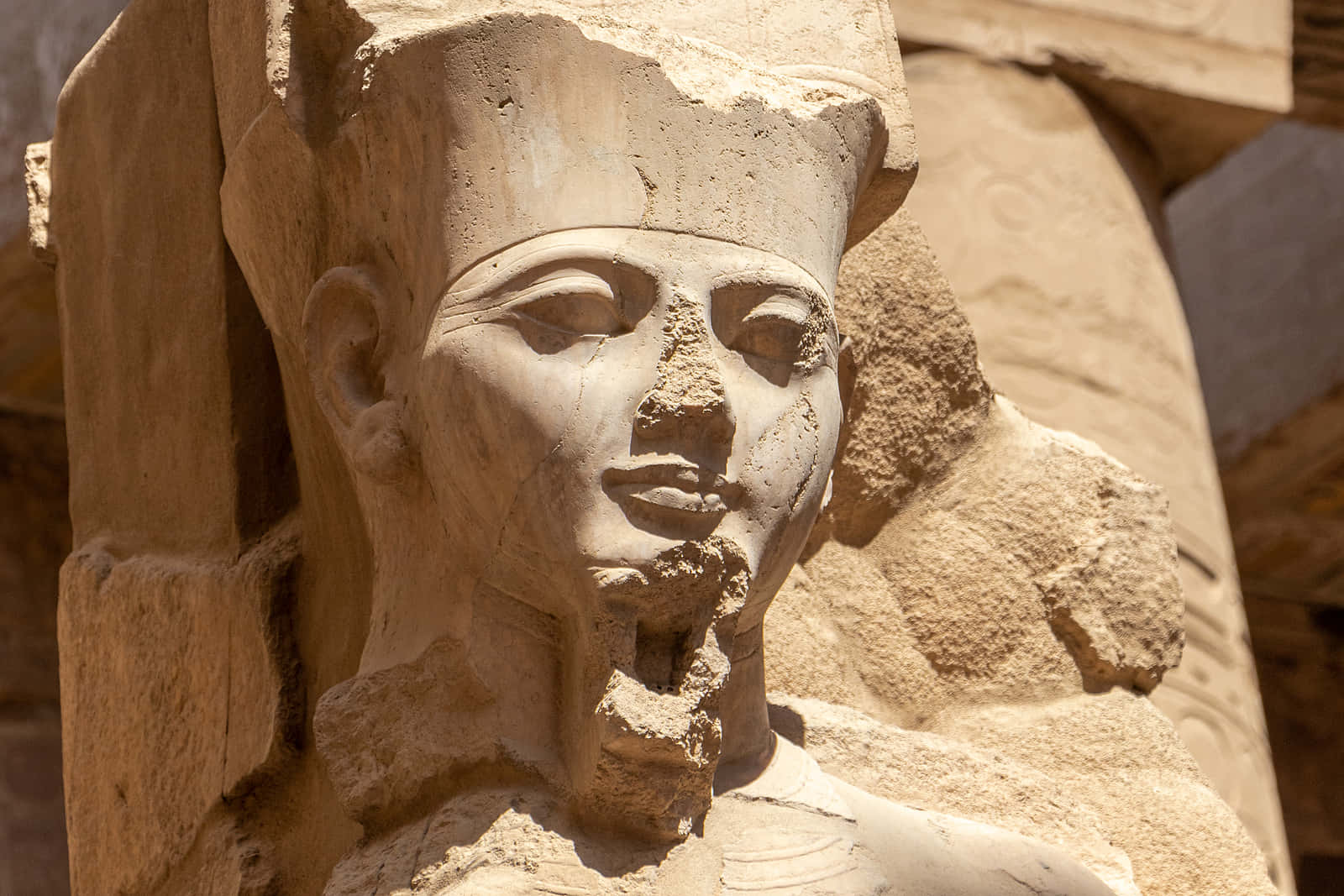 Ancient Egypt 桌布 壁紙 — 古埃及石像頭部特寫，具有風化特徵和傳統頭飾，在明亮陽光下。