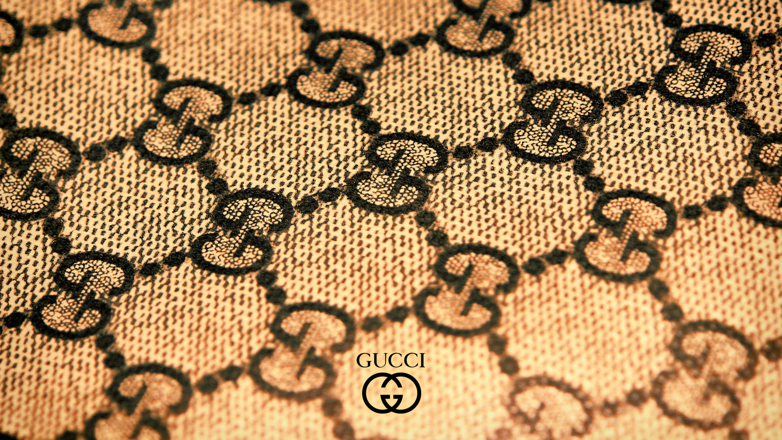 古奇紋樣與品牌標誌 壁紙 — Gucci 標誌性互鎖 G 字母組合圖案的特寫，呈現在帶有溫暖照明的紋理米色布料上。