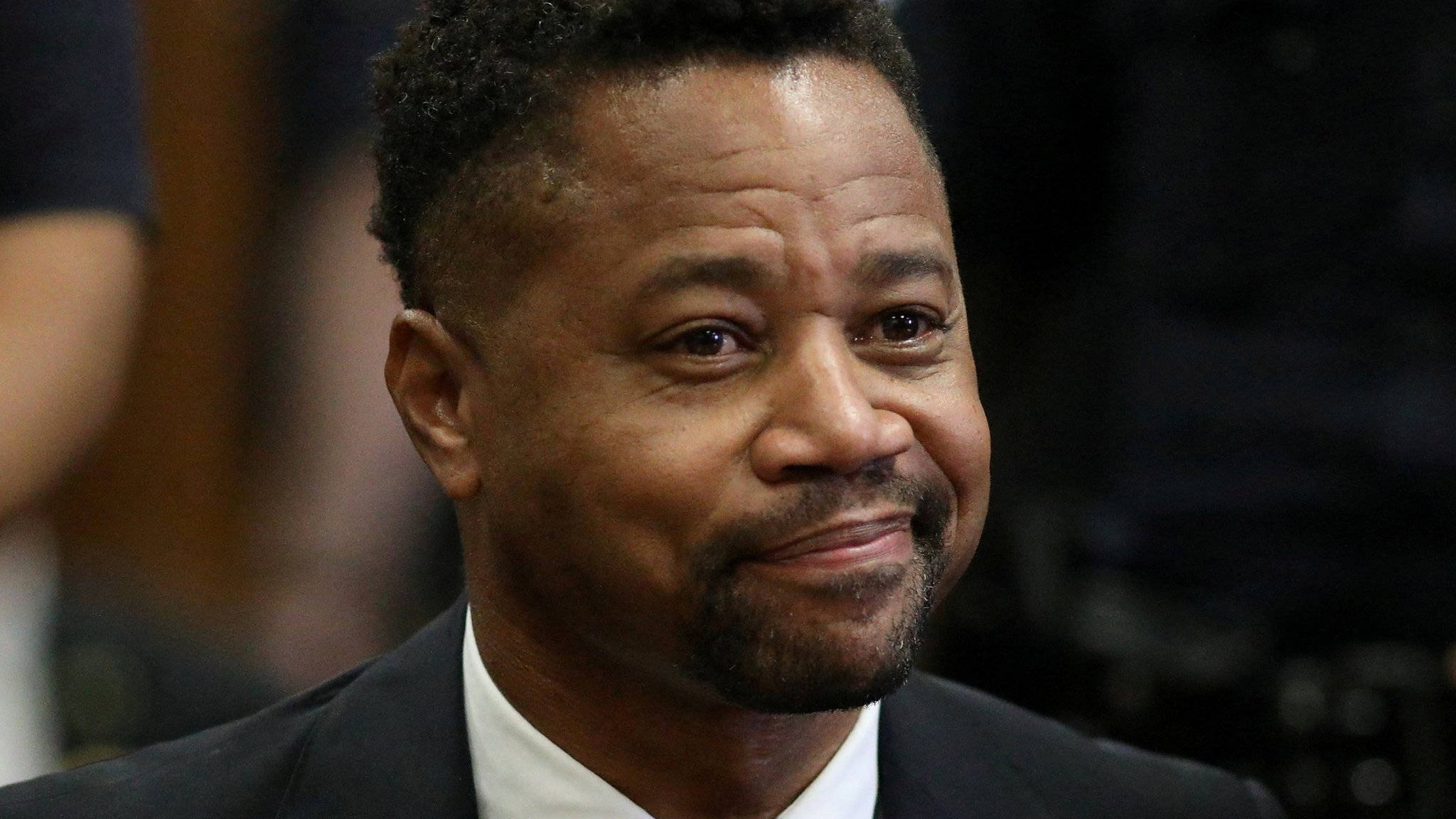 古巴·古丁 Jr. 獨照 壁紙 — 一位微笑的黑人男子身穿深色西裝和白襯衫的 close-up 肖像，背景為模糊的室內環境。