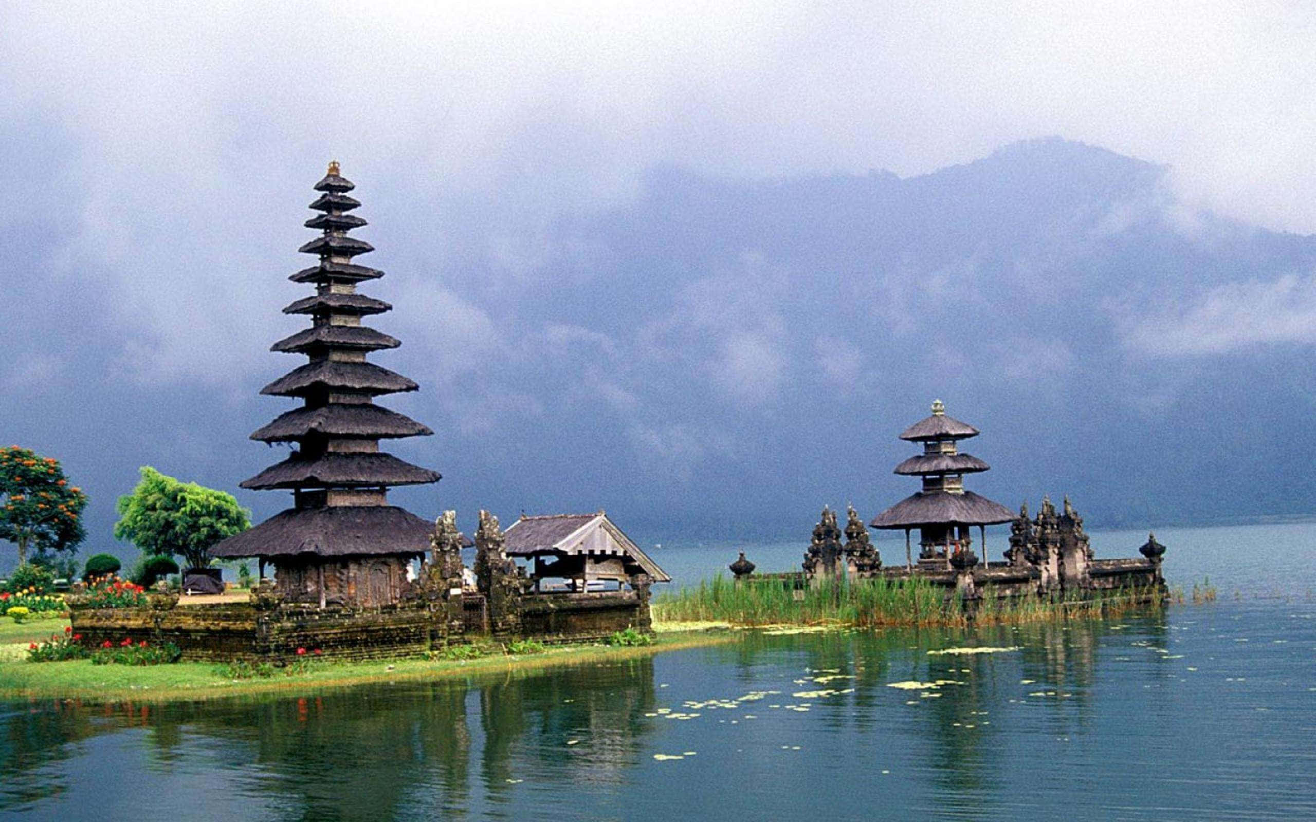 Bali Beach 桌布 壁紙 — 古老的巴厘島分層寺廟從平靜的湖面升起，周圍環繞著多霧的山脈，天空多雲。