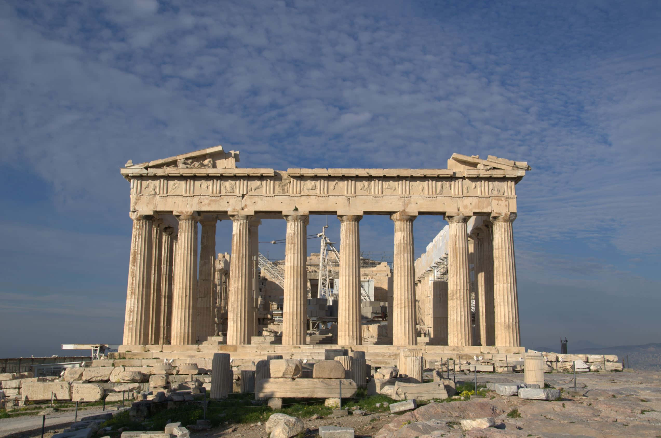 greek 桌布 壁紙 — 古老的帕德嫩神廟在明亮的藍天白雲下雄偉地矗立，其石柱和廢墟沐浴在溫暖的陽光中。