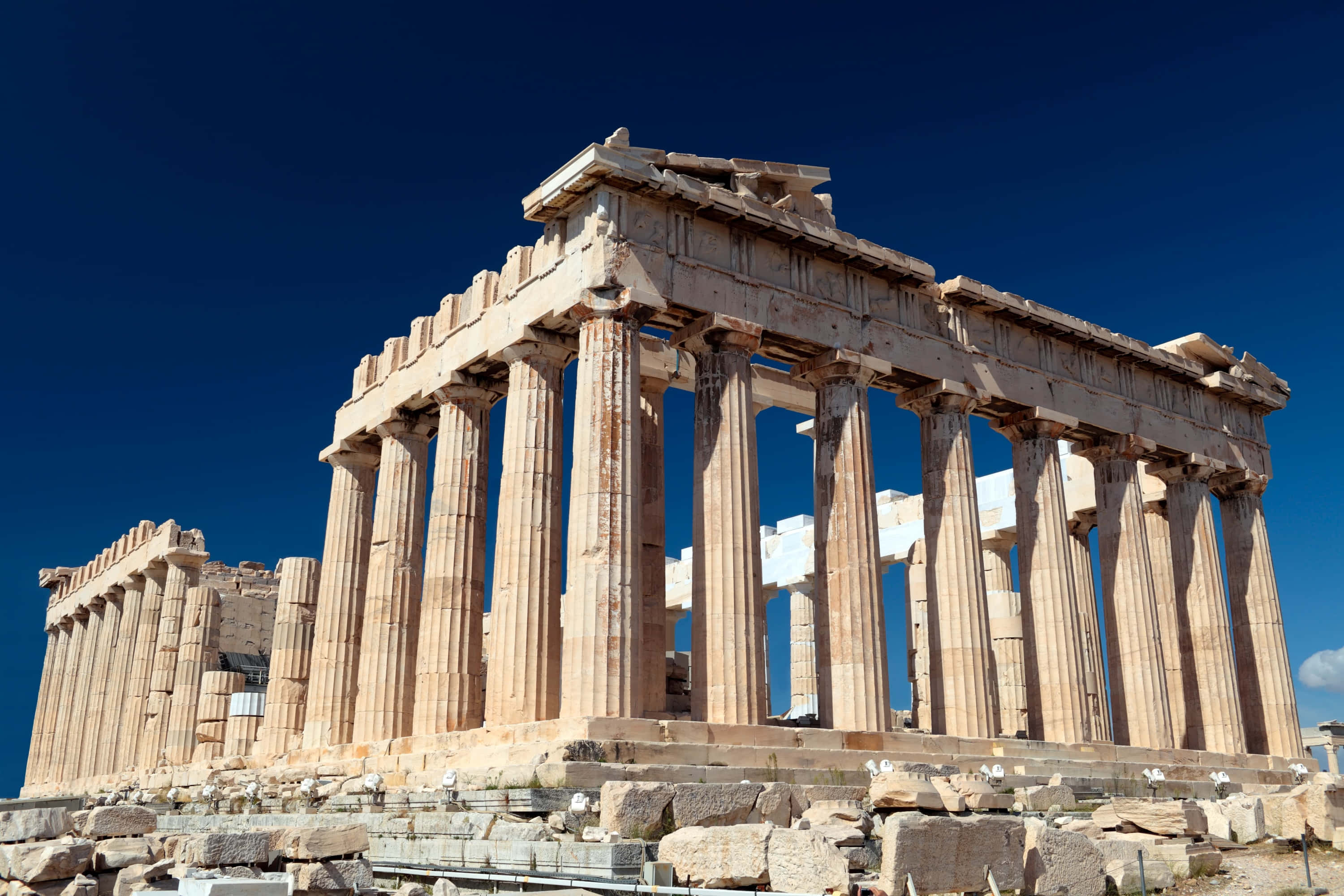 greek 桌布 壁紙 — 古老的帕德嫩神廟在深藍色的天空下雄偉地矗立，陽光照射的石柱和散落的廢墟。