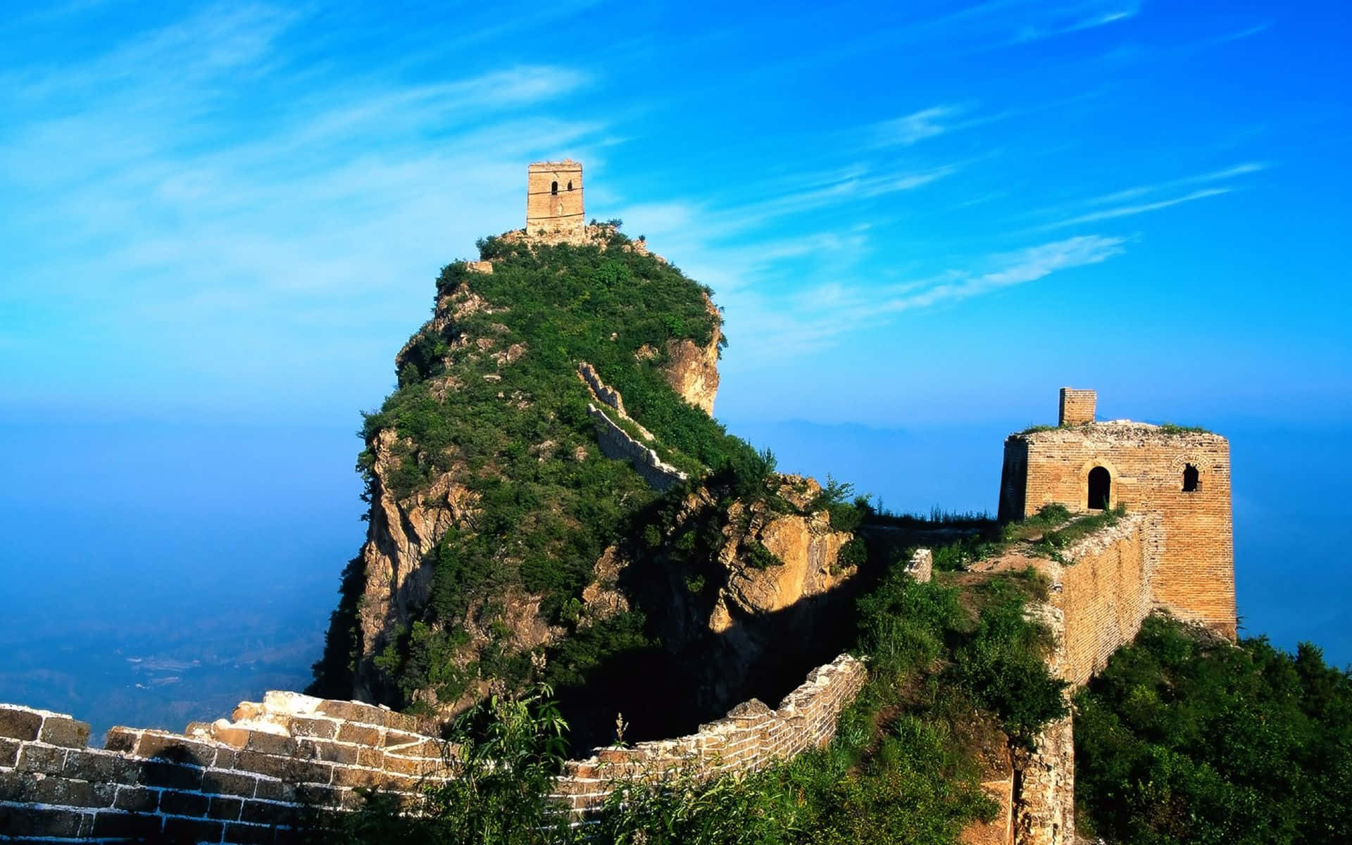 Beautiful Travel 桌布 壁紙 — 古老的石造長城城樓在鬱鬱蔥蔥的綠色山脊上雄偉地聳立，背景是帶有縷縷白雲的鮮豔藍天。