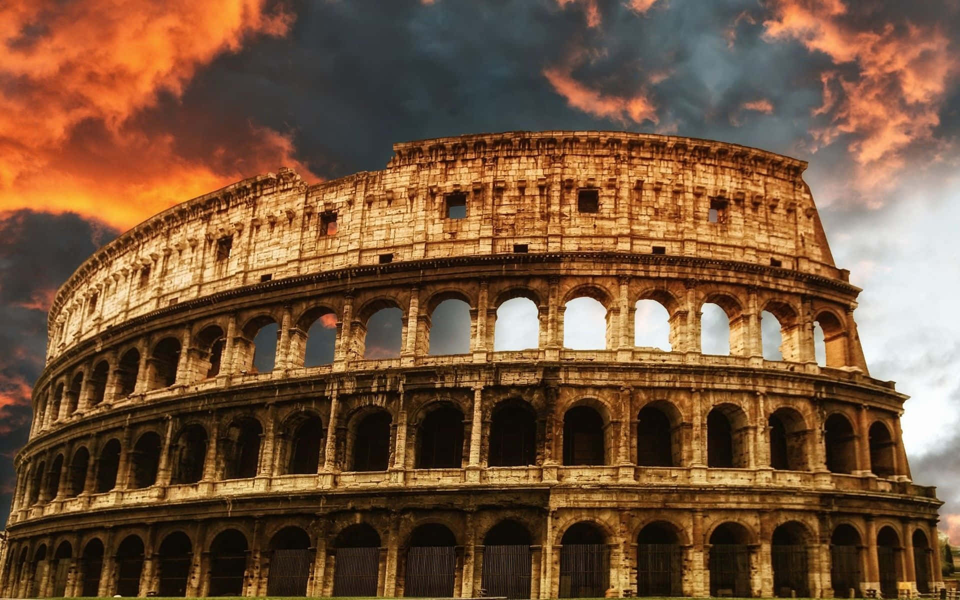 Rome 桌布 壁紙 — 古老的羅馬鬥獸場在火紅的夕陽天空下雄偉地矗立，伴隨著戲劇性的橙色和深色雲彩。