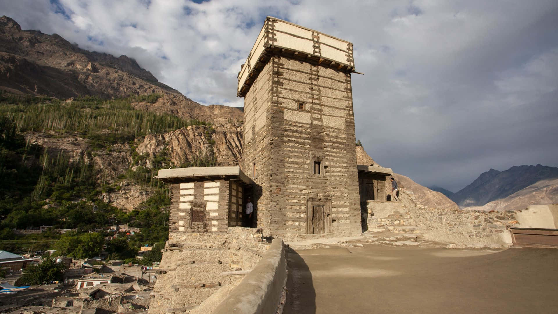 Fort 桌布 壁紙 — 古老石塔高聳於崎嶇山脈前，天空多雲，下方村莊依偎。