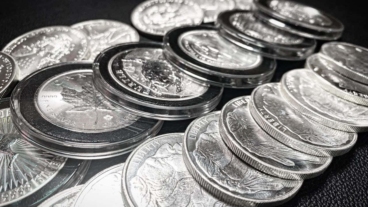 古舊銀幣 壁紙 — 堆疊的銀幣帶有精細雕刻，在聚焦光線下於深色紋理背景上閃閃發光。