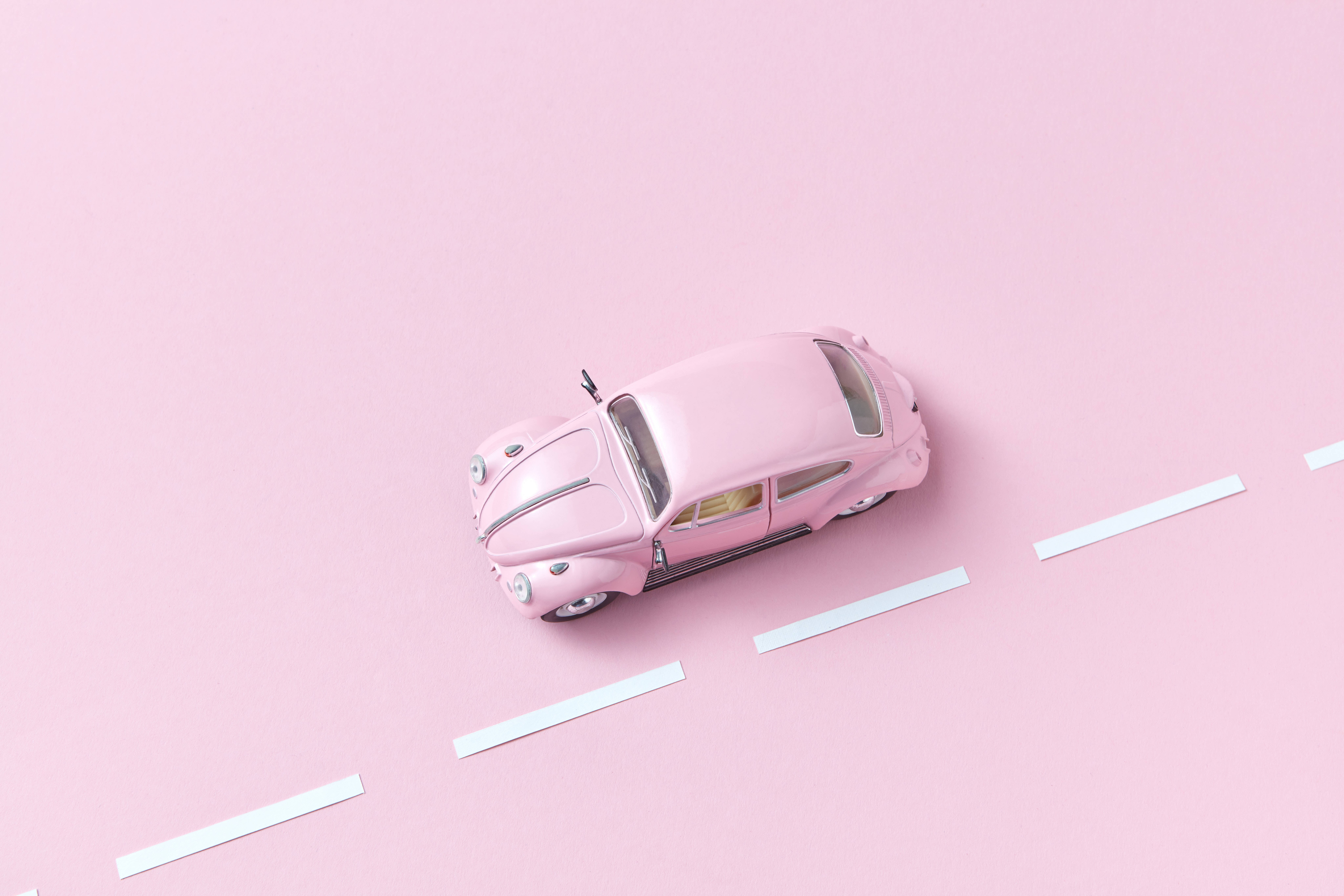 古董汽車在粉紅背景上 壁紙 — 一輛粉紅色的福士甲蟲玩具車放在一個極簡的粉紅色表面上，帶有白色虛線道路標線。