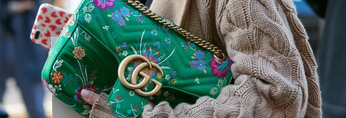 米色毛衣上綠色花卉手袋的特寫，帶有金色標誌。