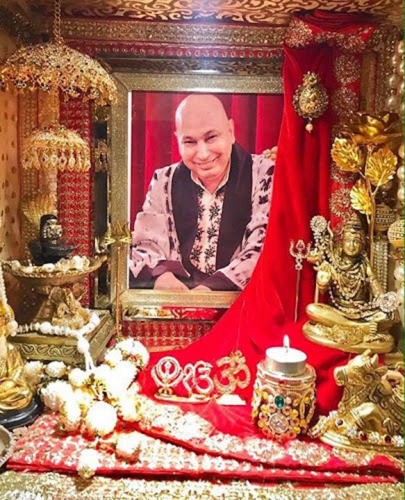 一個裝飾華麗的宗教神殿，有金色雕像、紅布和一個微笑男子的裱框肖像。