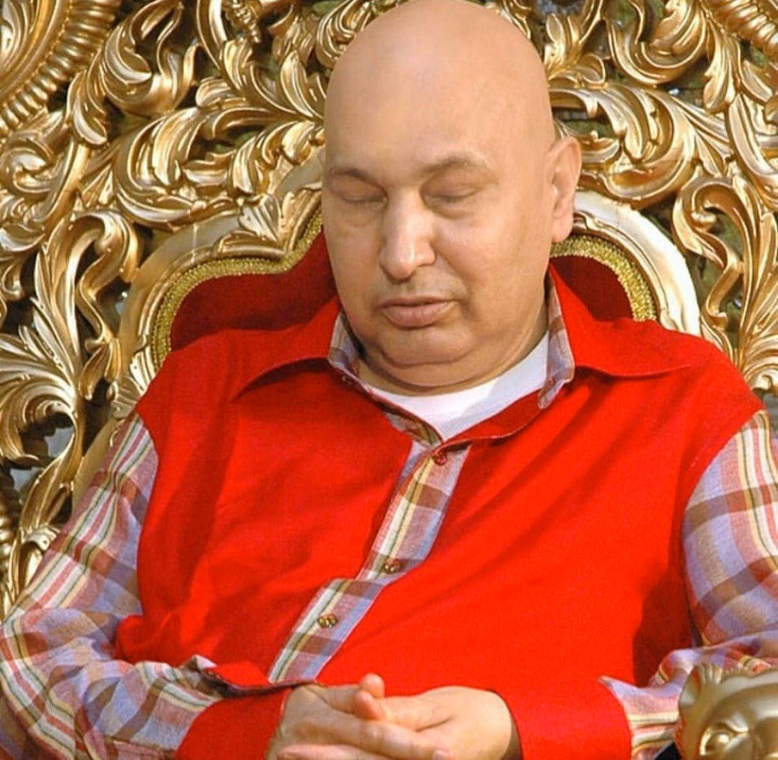 一個光頭男人穿著紅色背心在華麗的金色王座上睡覺。
