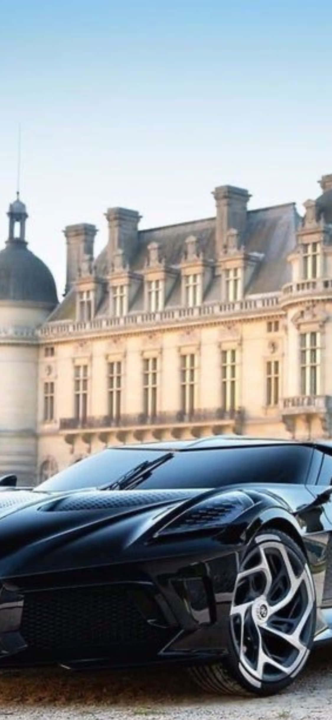 可在 iPhone Xs 壁紙上自訂 Bugatti Chiron Super Sport 300+ 壁紙 — 一架時尚黑色跑車停泊在宏偉的歐洲城堡前，背景是晴朗的藍天。