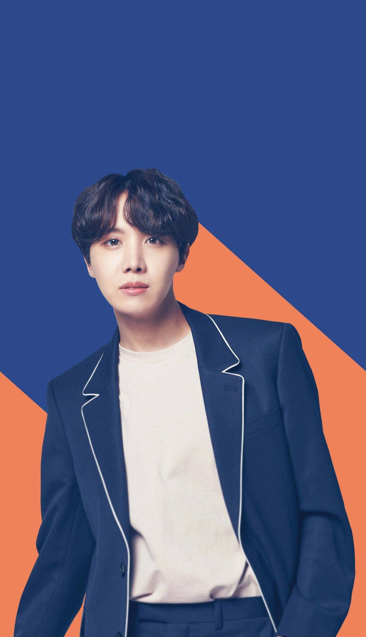 可愛BTS J-Hope藍橙抽象背景 壁紙 — 一位身穿海軍藍色西裝外套（白色飾邊）的年輕男子站在大膽的藍色和橙色幾何背景前。