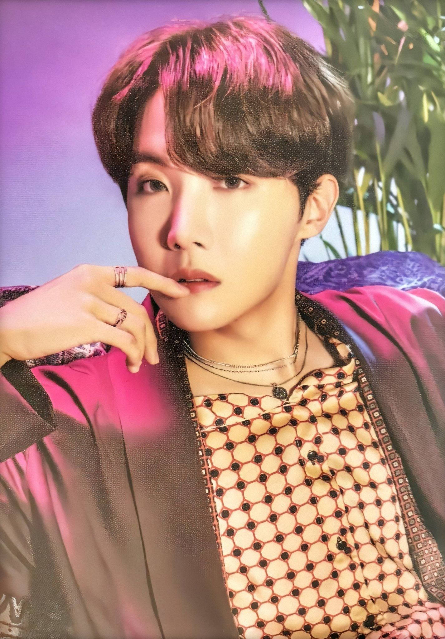 可愛BTS J-Hope身穿棕色上衣 壁紙 — 一位帶粉紅色頭髮的年輕男子在紫色背景和綠色樹葉前沉思地擺姿勢。