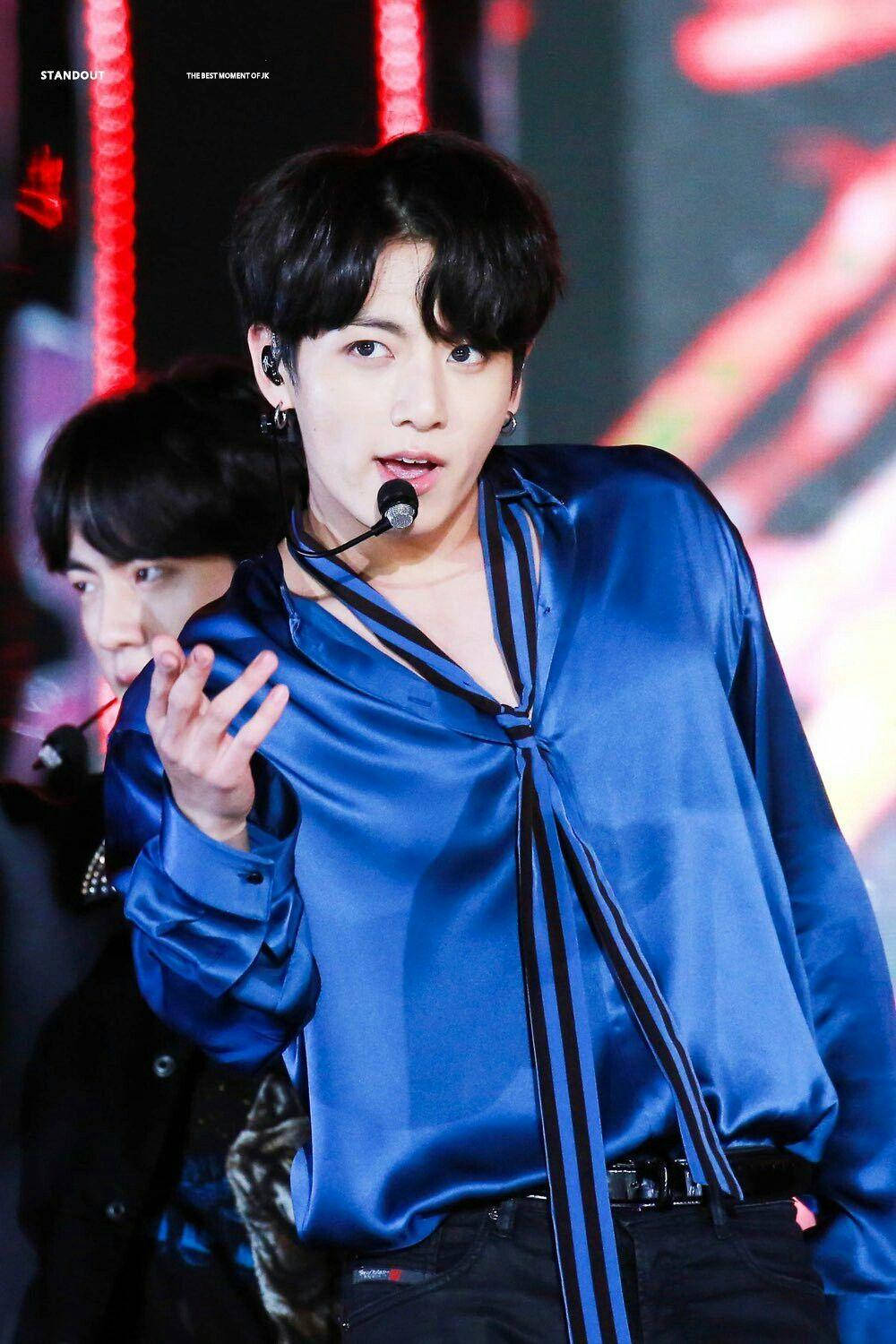 可愛BTS JK演唱會演出 壁紙 — 一位身穿閃亮藍色緞面襯衫的男性表演者在燈光明亮的舞台上做手勢，舞台上有紅燈，身後還有另一位藝術家。