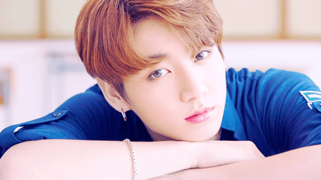 可愛BTS Jungkook近照 壁紙 — 一位紅褐色頭髮的年輕男子，身穿藍色襯衫和銀飾，將下巴擱在手臂上。