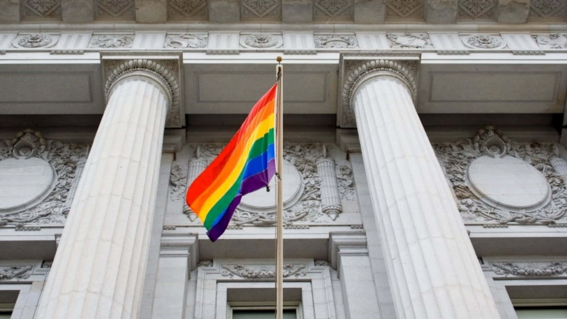 可愛LGBT彩虹旗與舊金山市政廳 壁紙 — 一面鮮豔的彩虹旗在高柱和華麗石雕的宏偉新古典主義建築背景下自豪地飄揚。