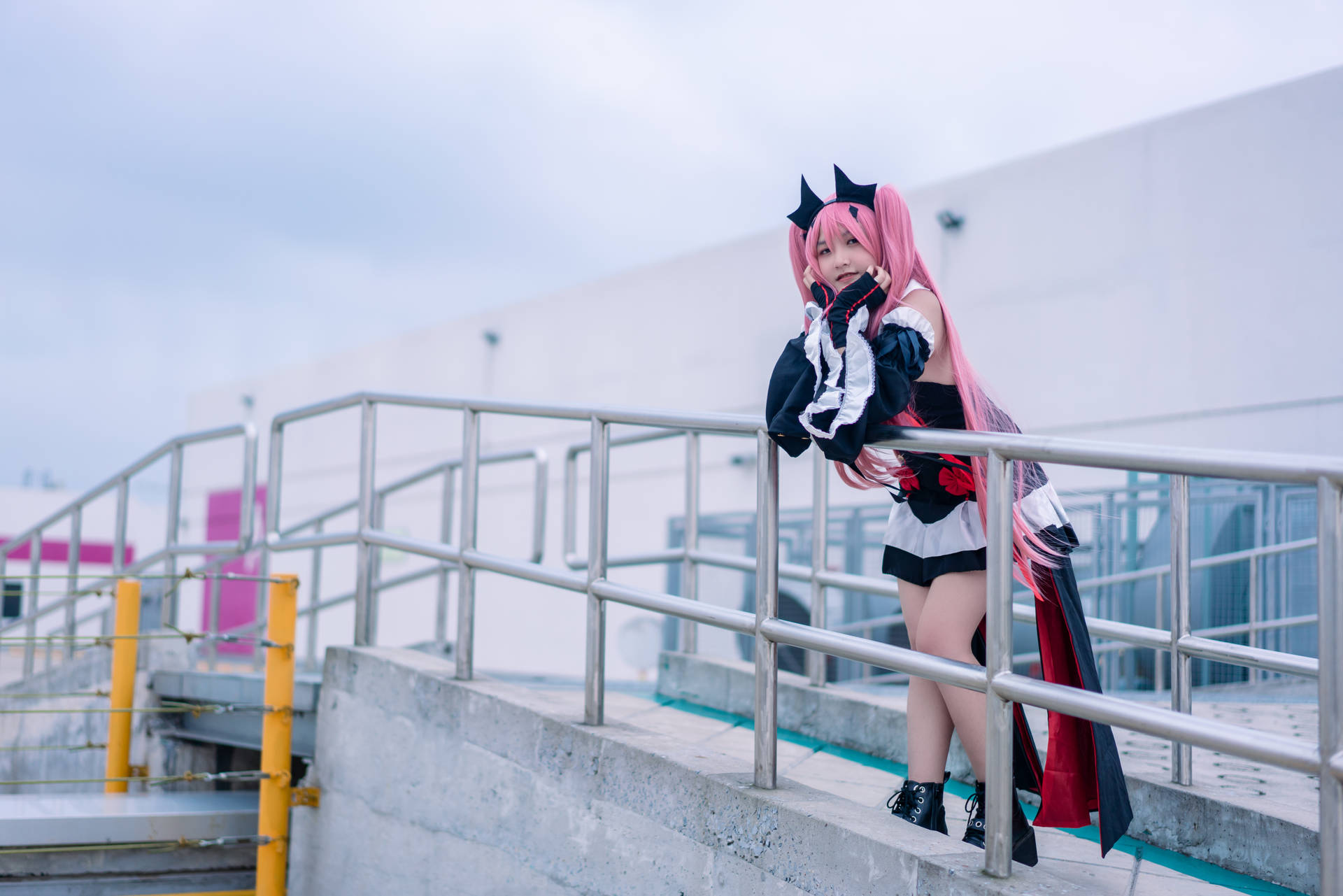 粉紅色頭髮的cosplayer穿著黑白服裝，在戶外靠著金屬欄杆。
