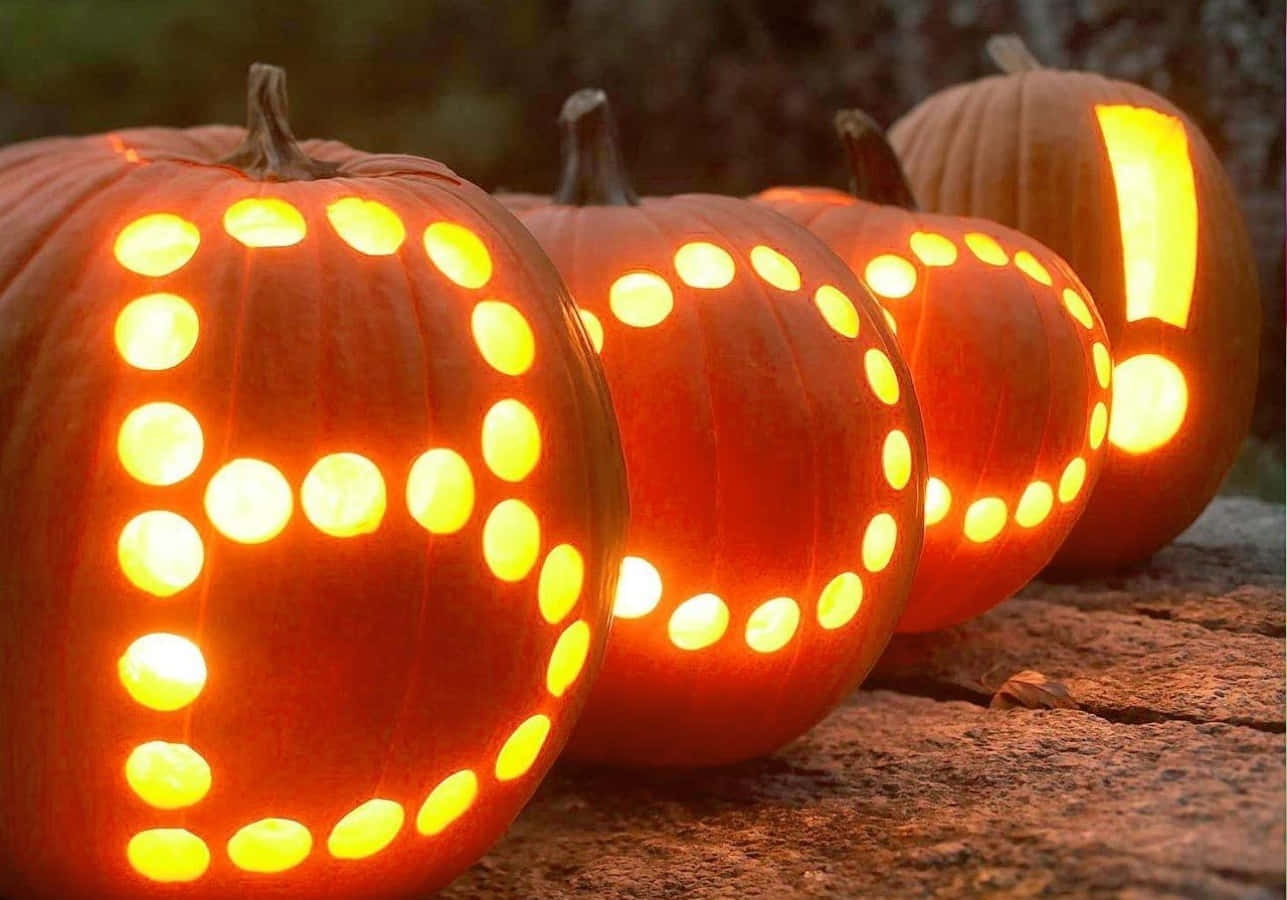 可愛南瓜雕刻「Boo」圖 壁紙 — 發光的南瓜雕刻著發光的點，拼出「BOO」和感嘆號，放在黃昏時分的石面上。