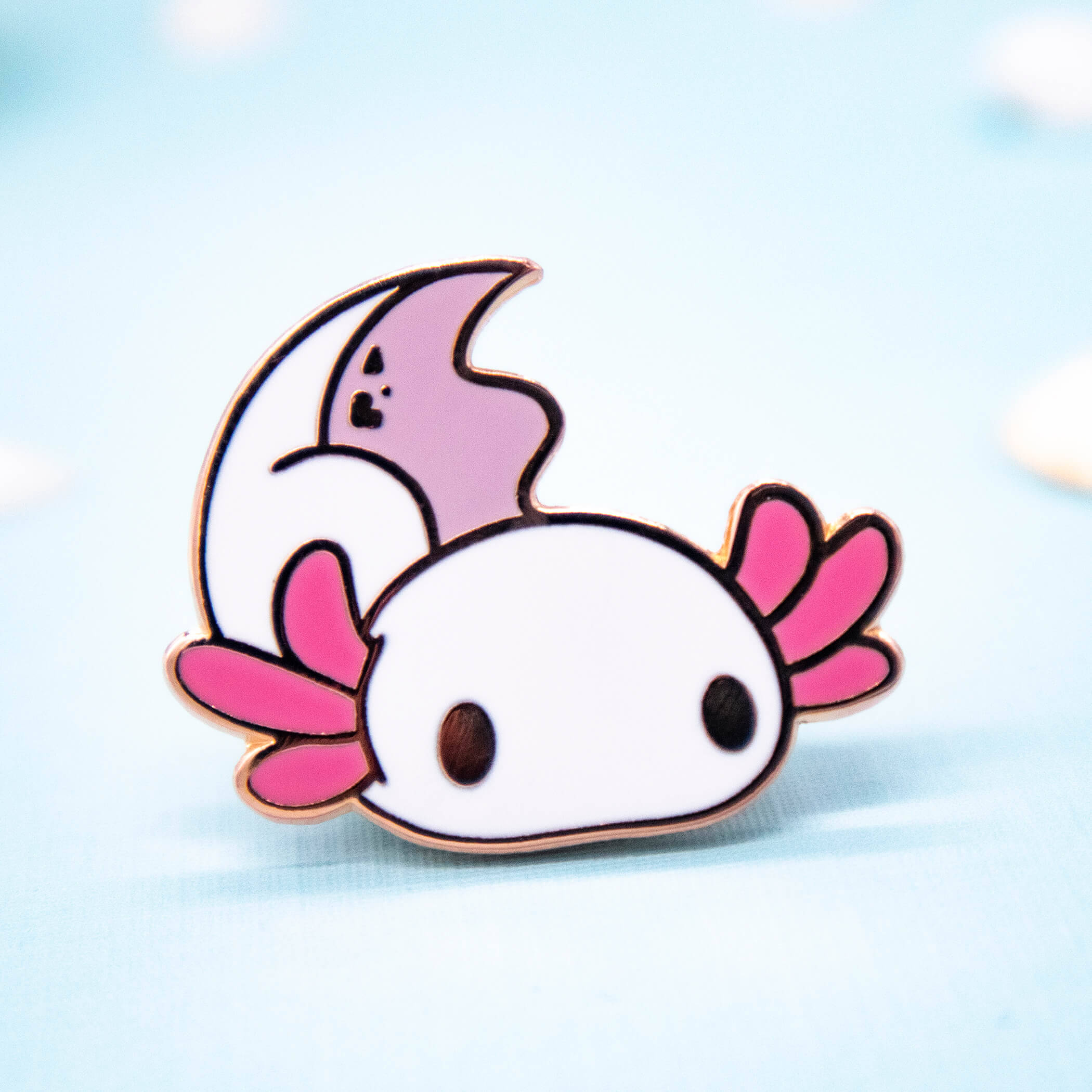 可愛卡通 Axolotl 貼紙 壁紙 — 一個可愛的卡通蠑螈琺瑯別針，帶有粉紅色鰓和月牙尾巴，放在柔軟的藍色表面上。