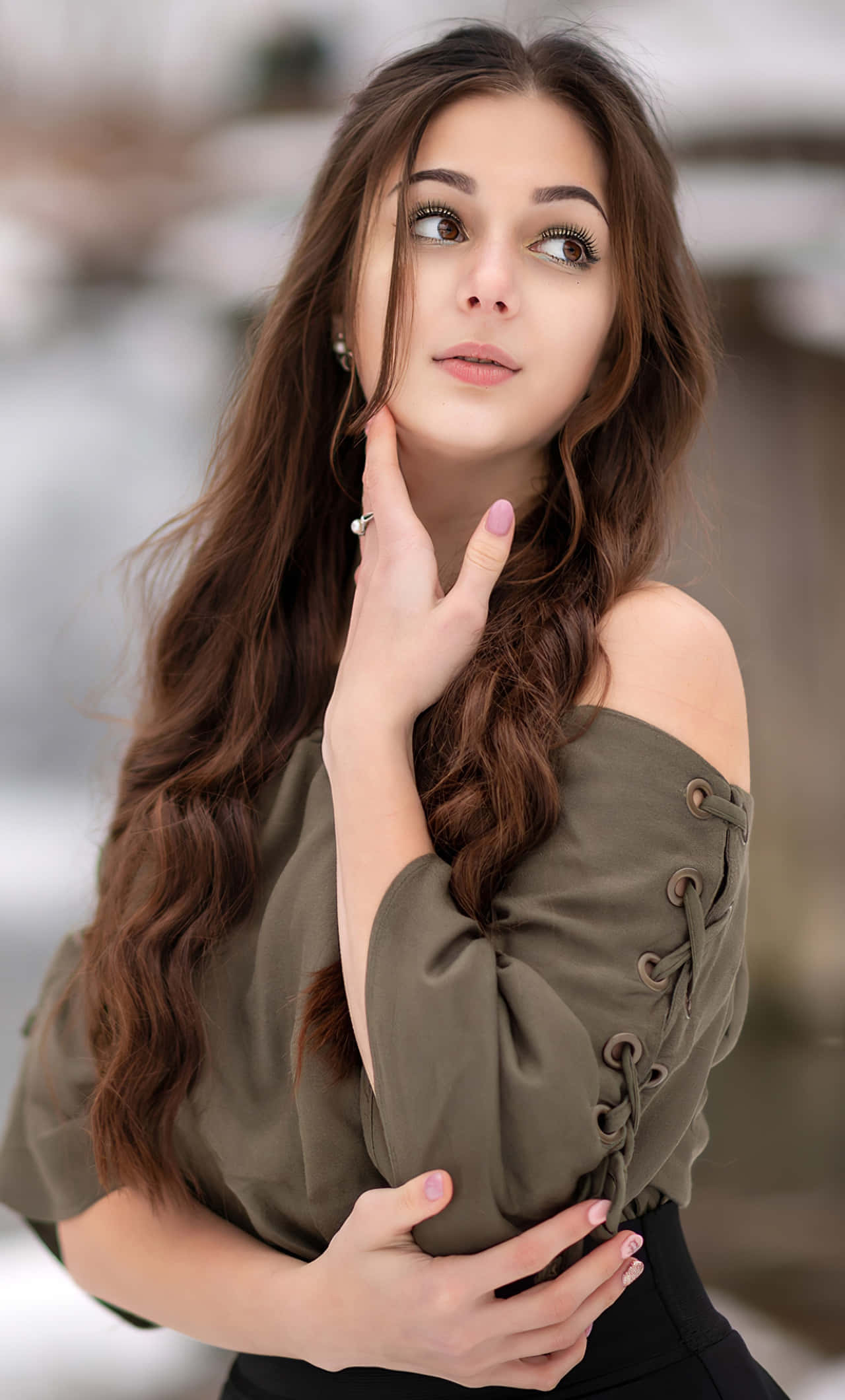 可愛女孩享受美好一天！ 壁紙 — 一位長棕髮的年輕女性在雪地戶外環境中向上凝視，身穿橄欖色露肩上衣。