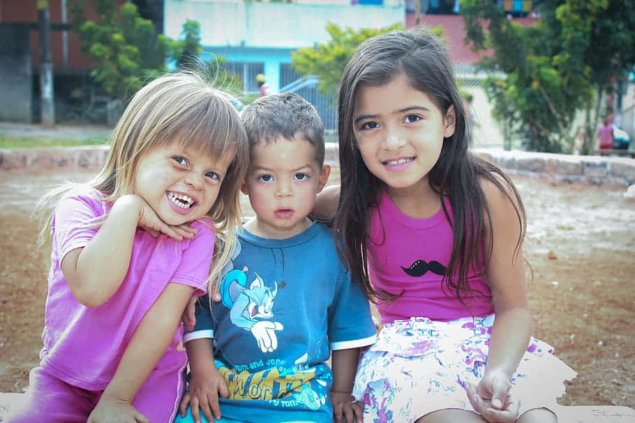 三個年幼的孩子在陽光明媚的戶外環境中笑著一起擺姿勢。