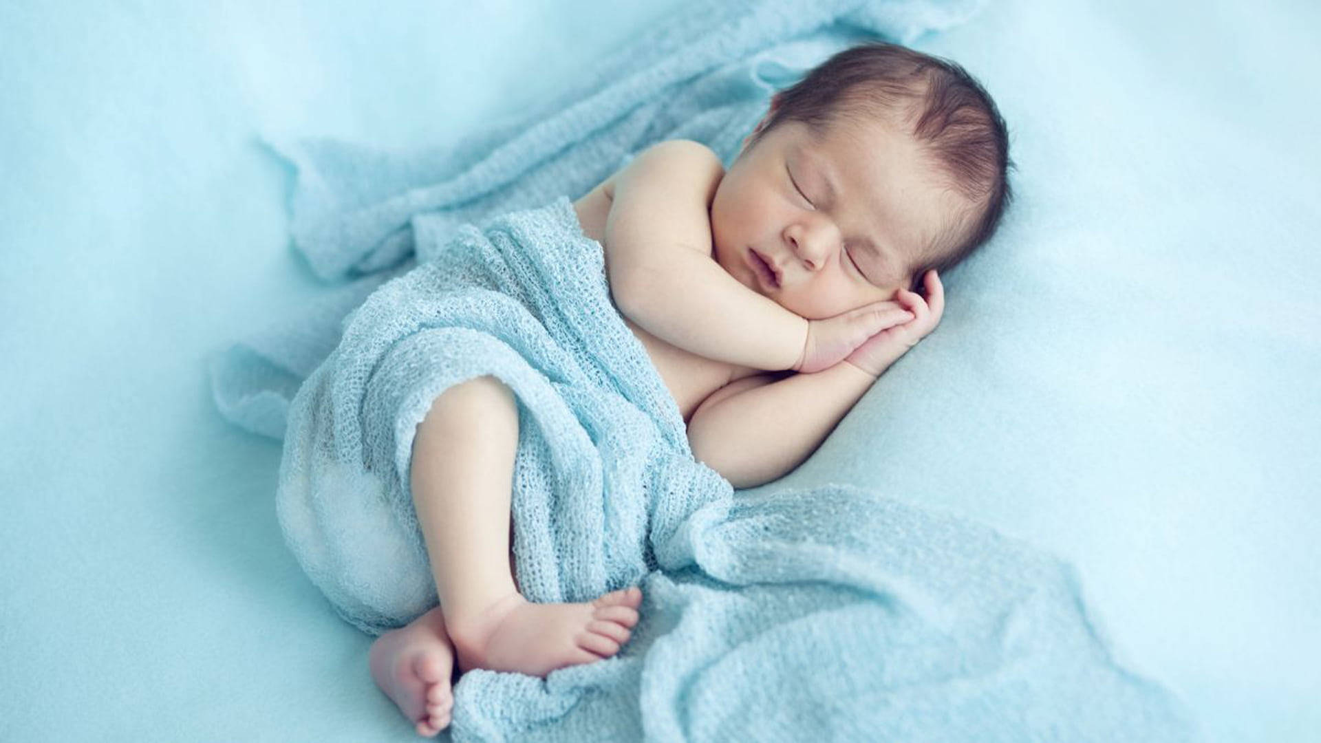 一個被柔軟藍色毯子包裹著睡覺的新生嬰兒。