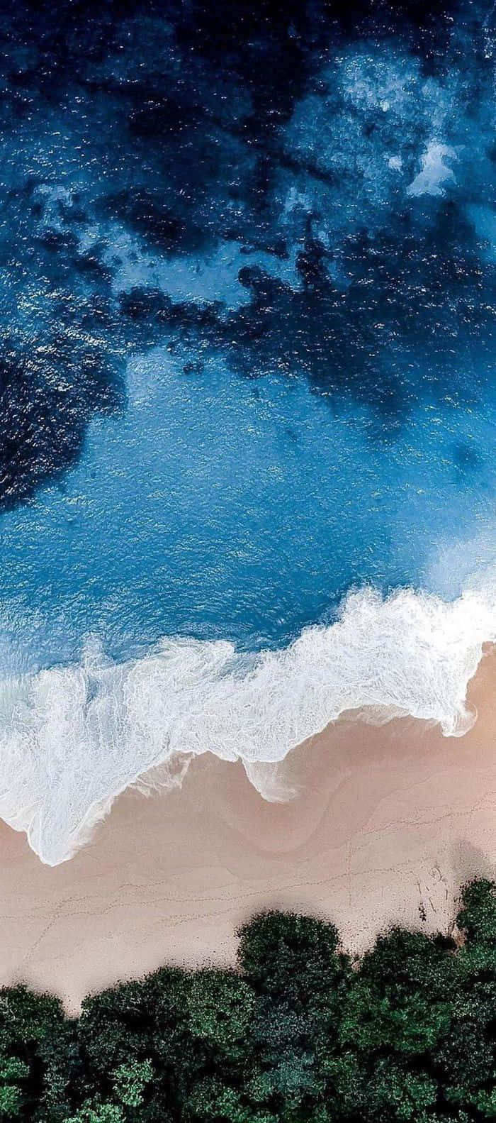 可愛孤寂夏日海灘空中俯瞰 壁紙 — 從空中俯瞰，綠松石色的海浪拍打著沙灘，沙灘邊緣被茂密的綠色植物環繞。