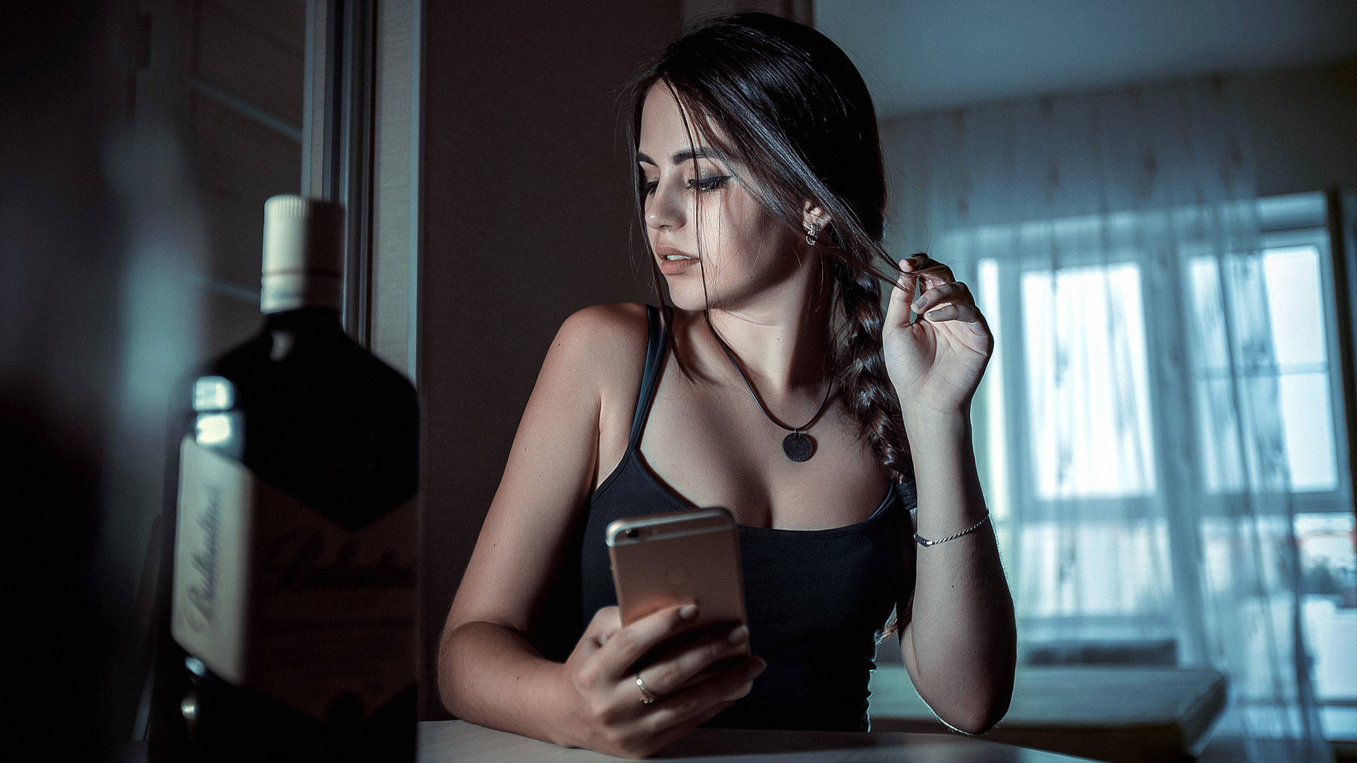 女人在昏暗房間裡拿著手機和酒瓶